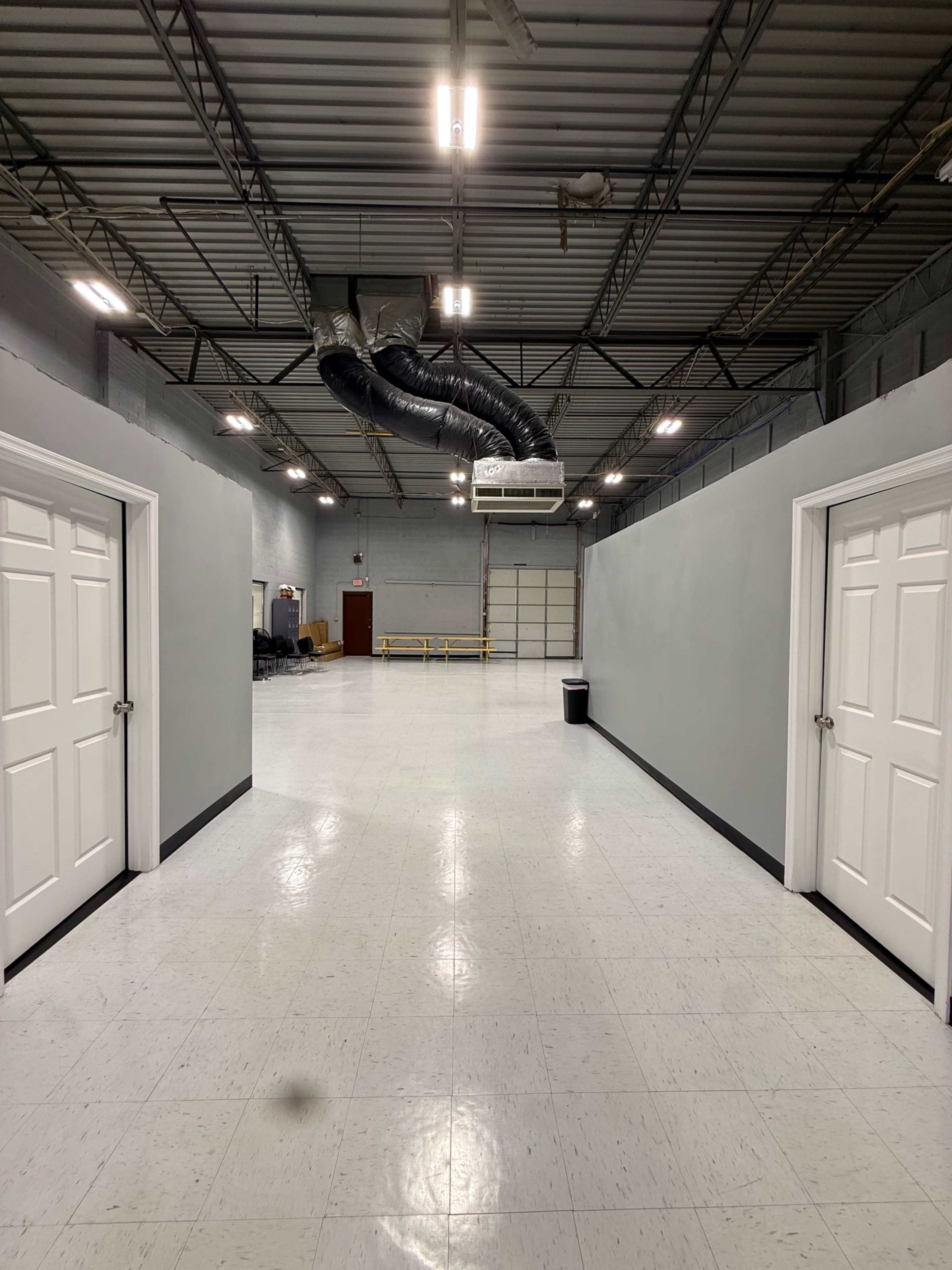 The image shows a spacious industrial hallway with two doors on either side and a ceiling-mounted air duct.