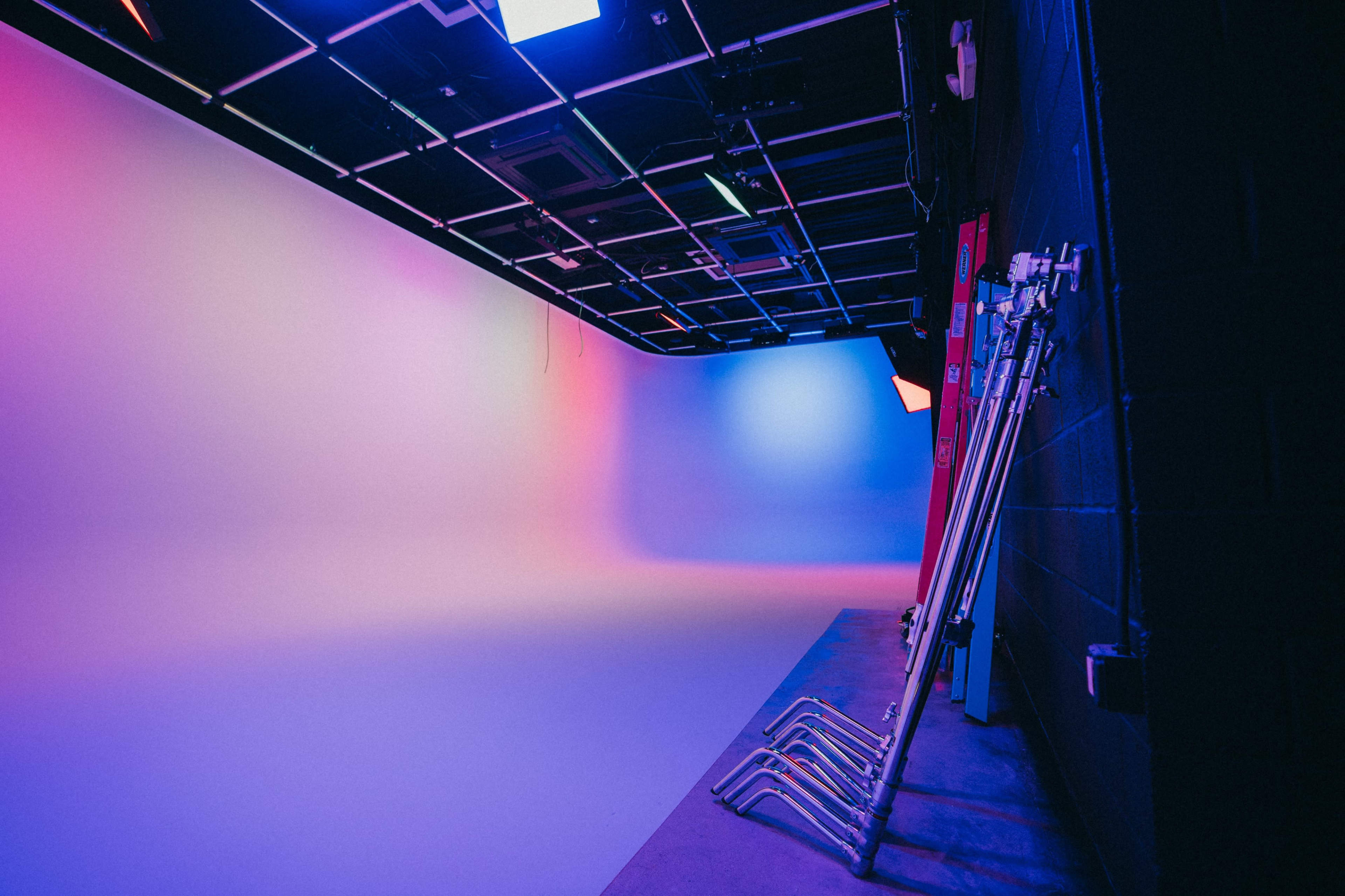 A studio space with a blank backdrop illuminated by colorful lights and several lighting stands against the wall.