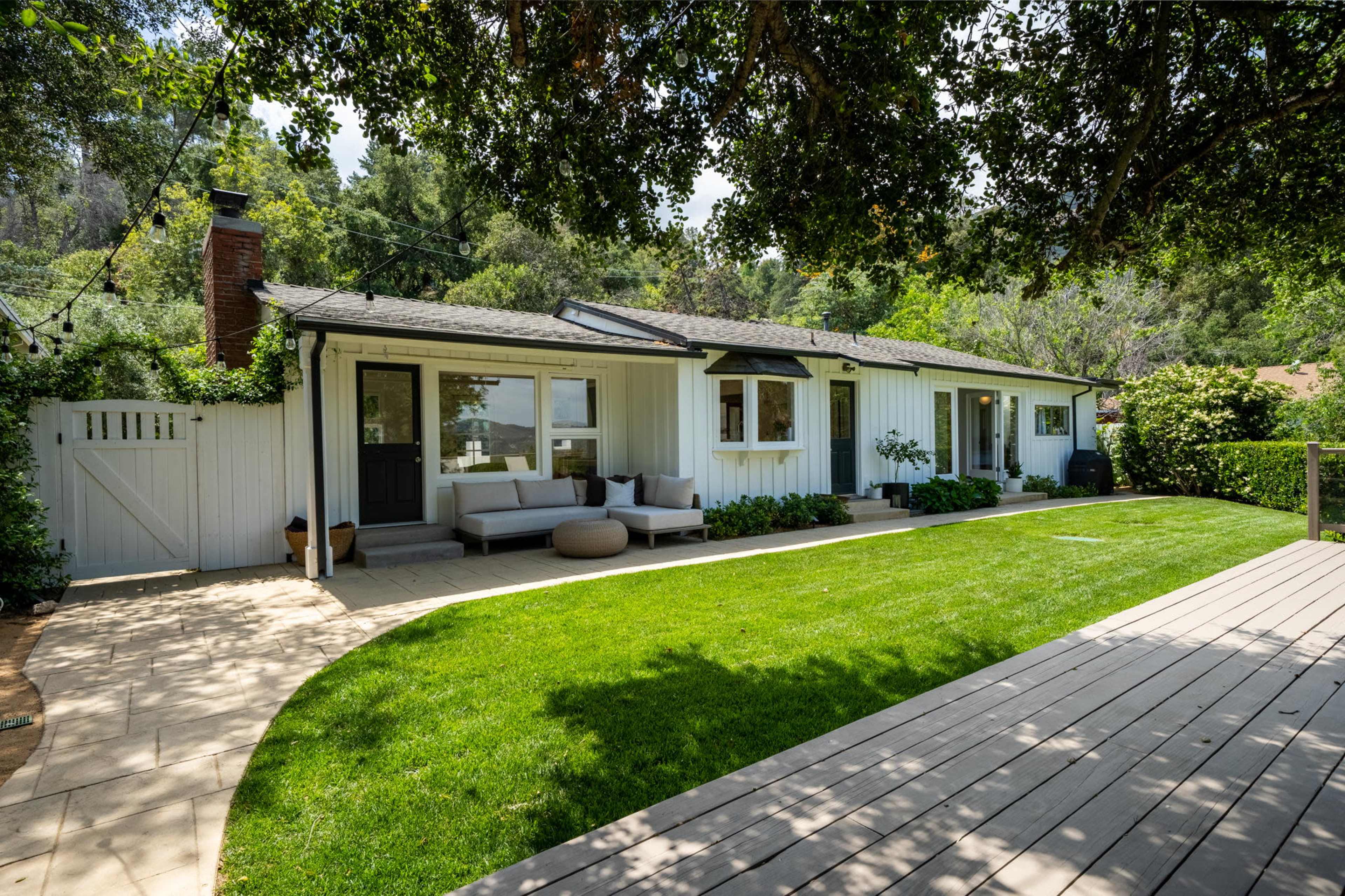 A single-story house with a landscaped yard and wooden deck is surrounded by trees and greenery.