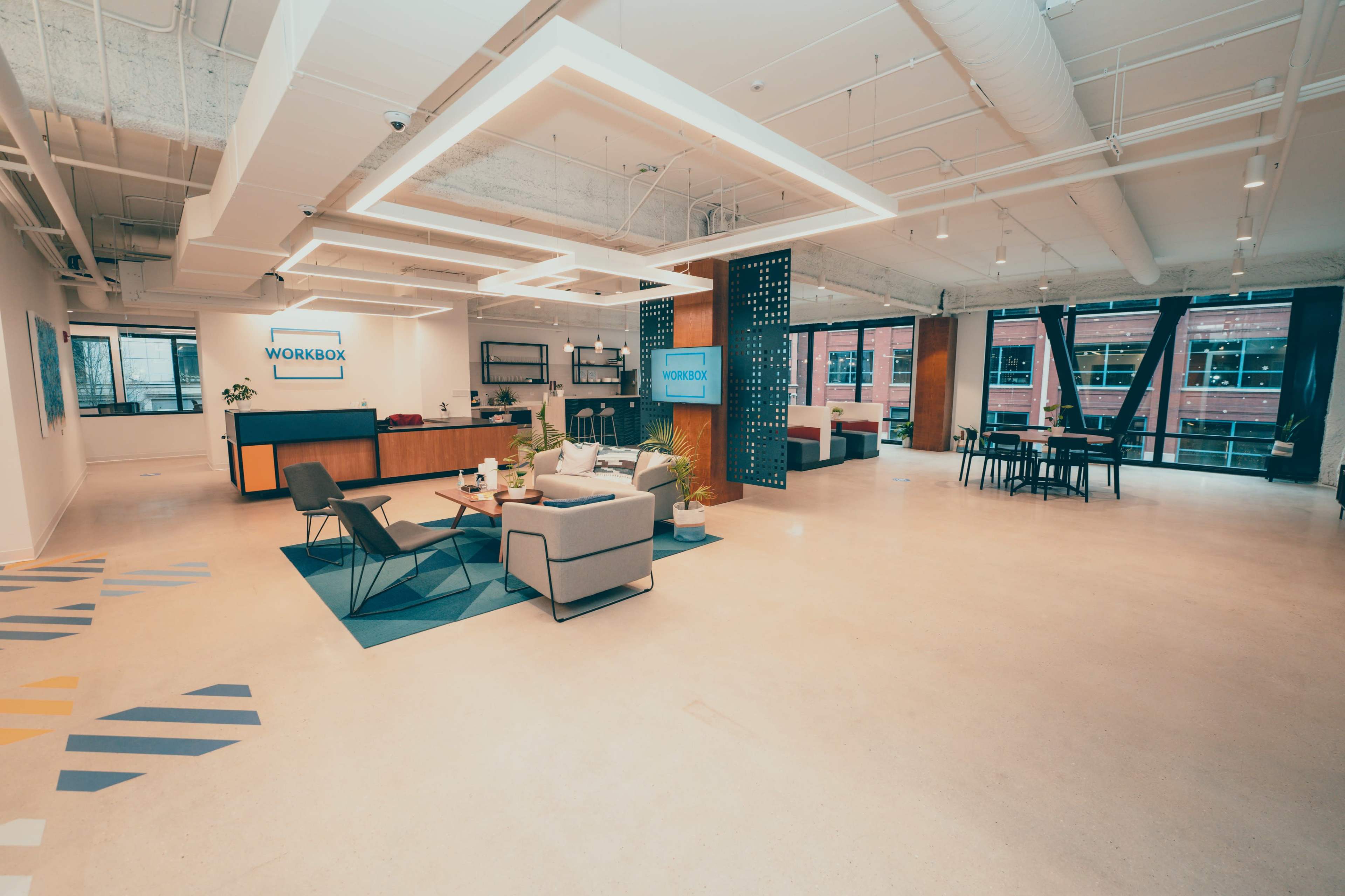 A modern office space with a reception area featuring seating, a coffee table, and a workspace with tables and chairs.