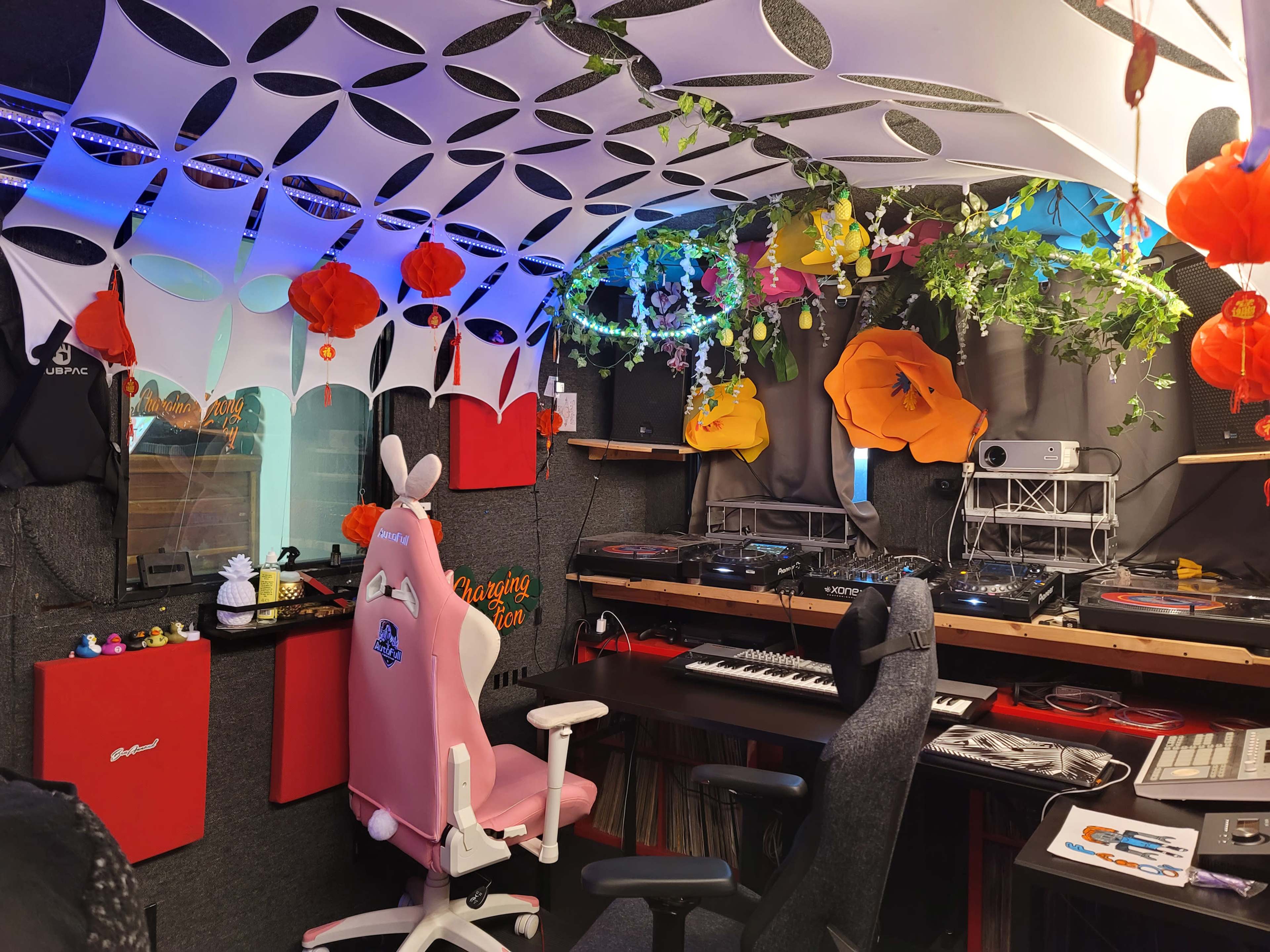 A decorated music studio with DJ equipment, colorful decor, and two ergonomic chairs.