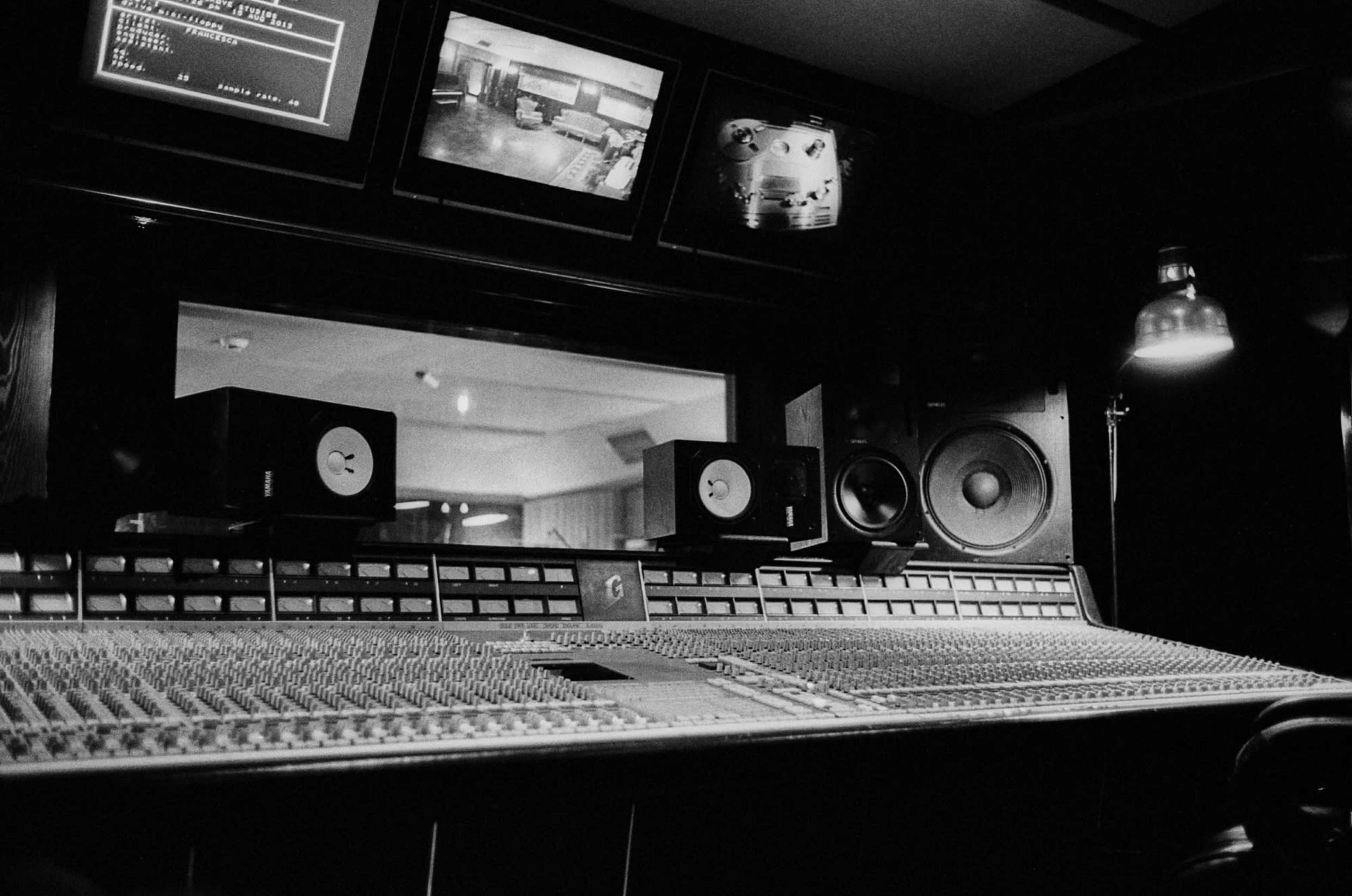 The image shows a recording studio control desk with multiple monitors and audio equipment.