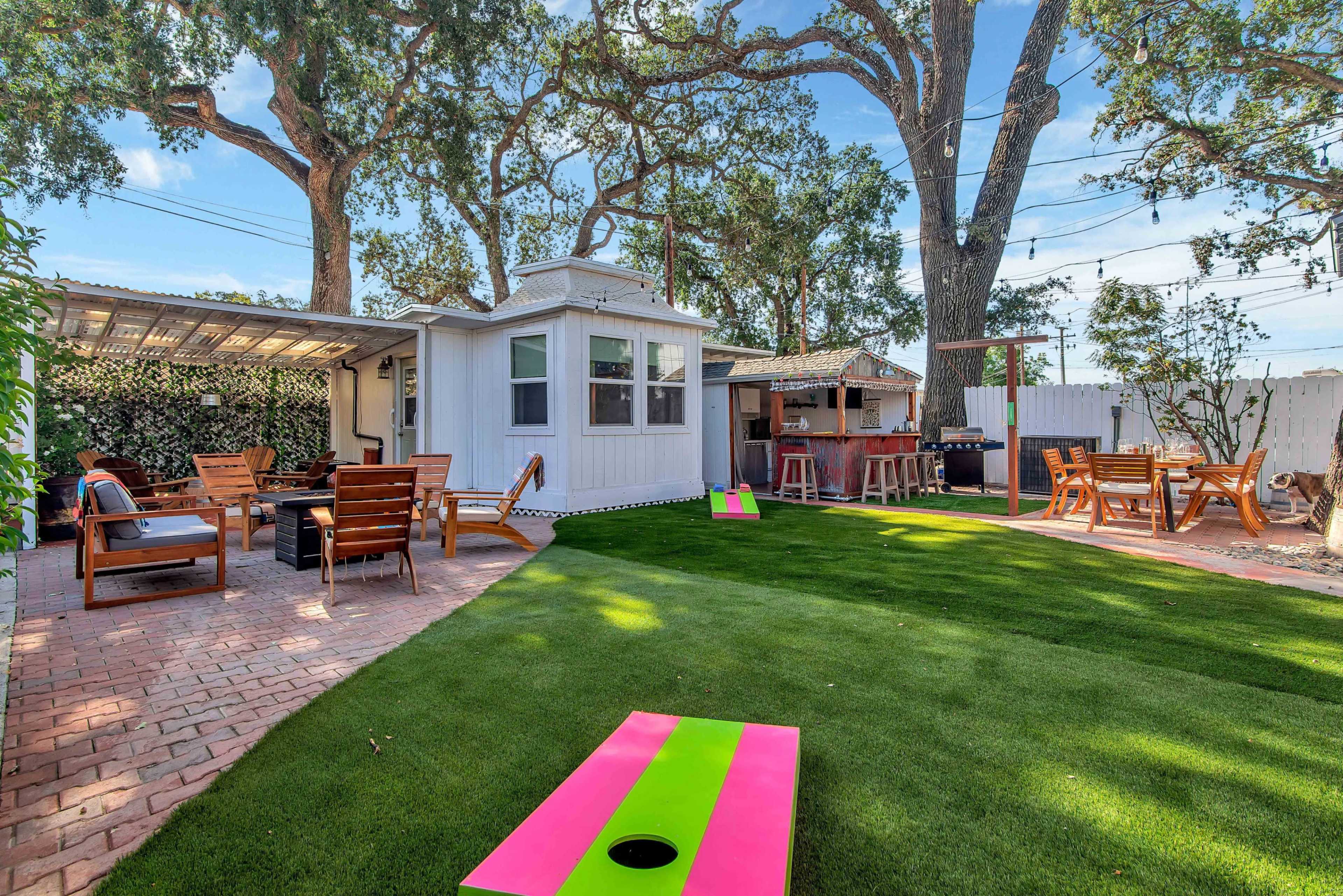 A backyard with a green lawn, a wooden seating area, a small white shed, and colorful cornhole boards.