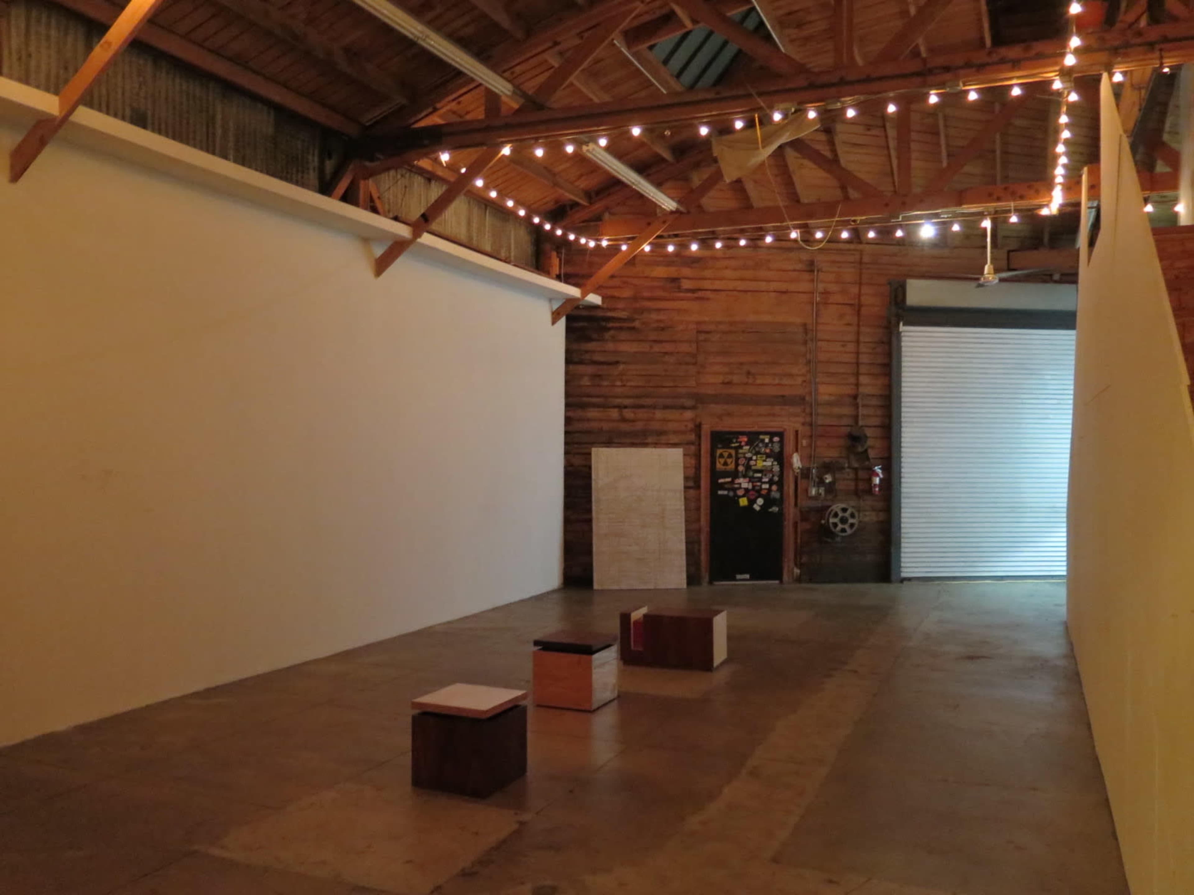 An empty art gallery with wooden beams, a concrete floor, and soft lighting from string lights above.