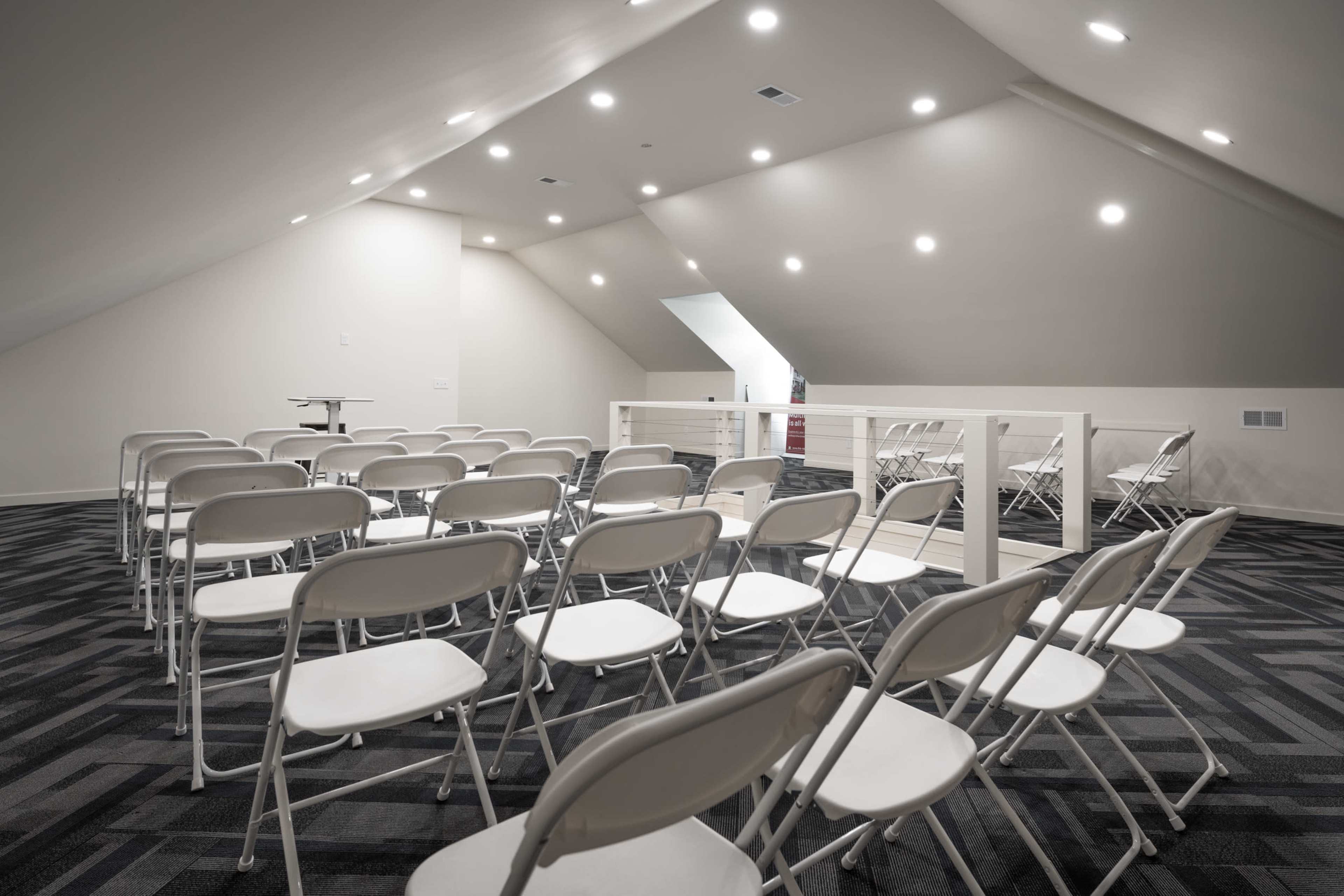 A spacious attic room with white folding chairs arranged in rows and bright ceiling lights illuminating the space.