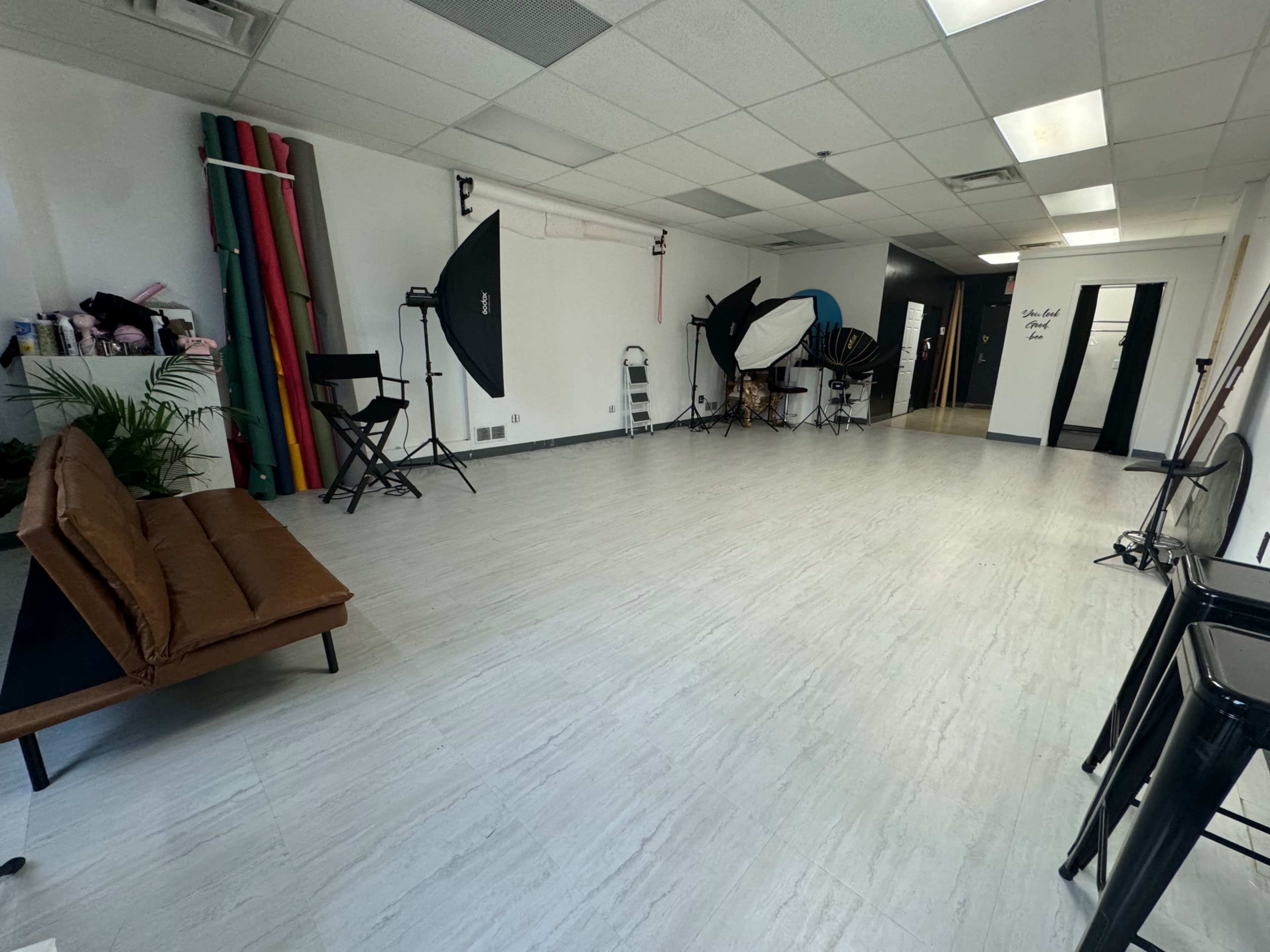 A spacious photography studio with various lighting equipment and backdrops, along with a brown couch and minimal decor.