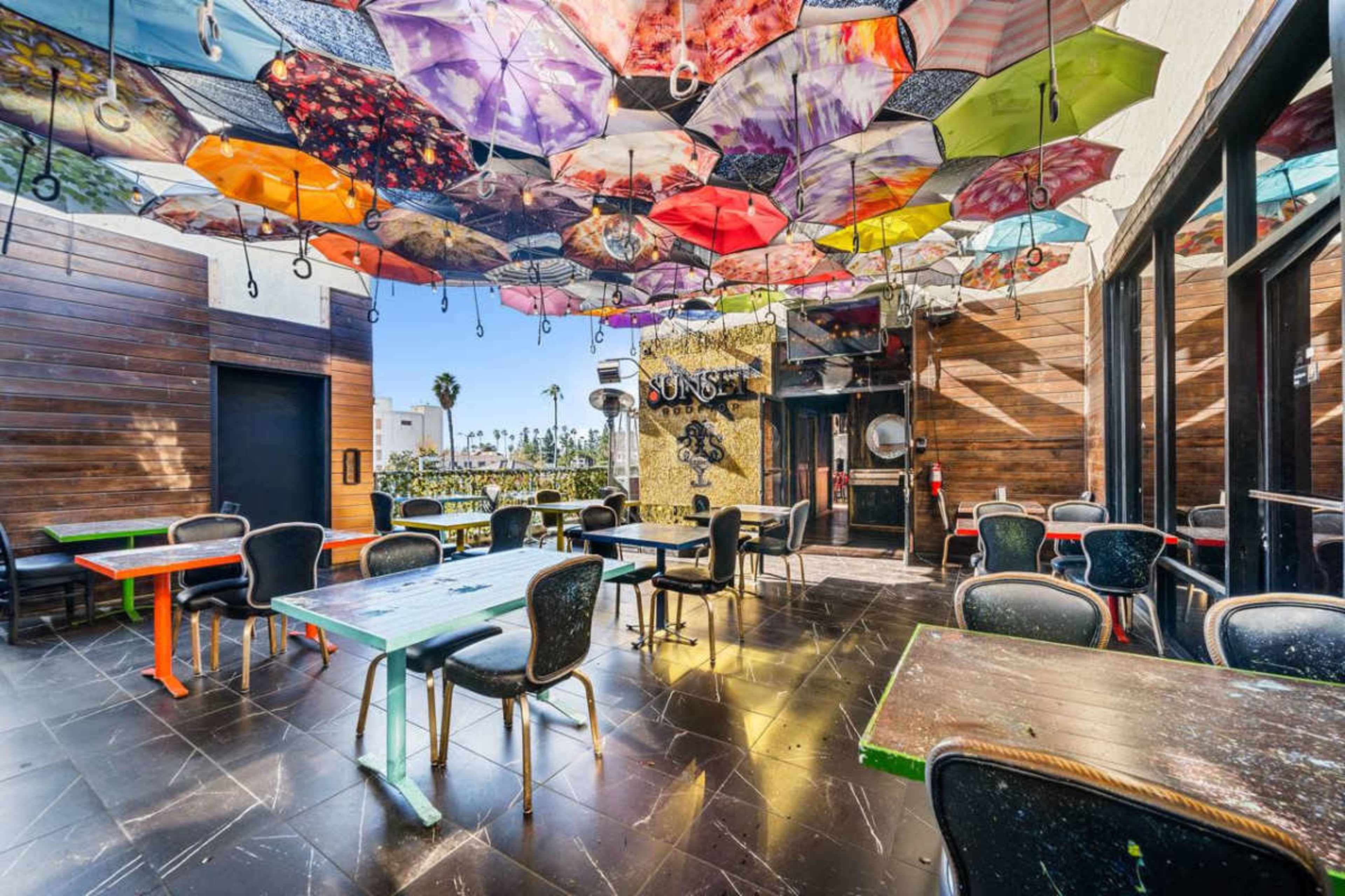 A restaurant interior features colorful umbrellas hanging from the ceiling above tables and chairs.