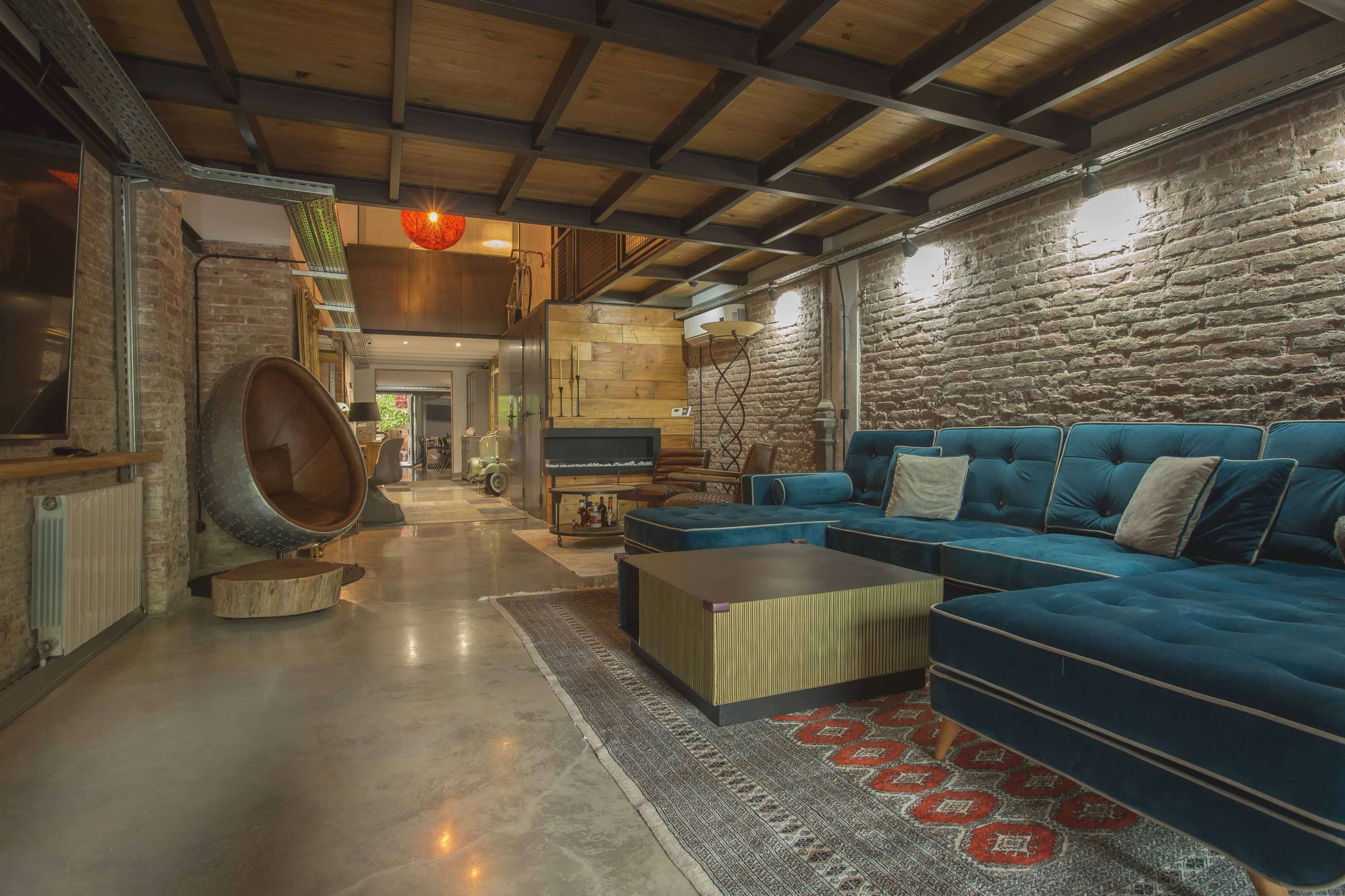 A modern living room with a blue sectional couch, a round chair, and exposed brick walls.
