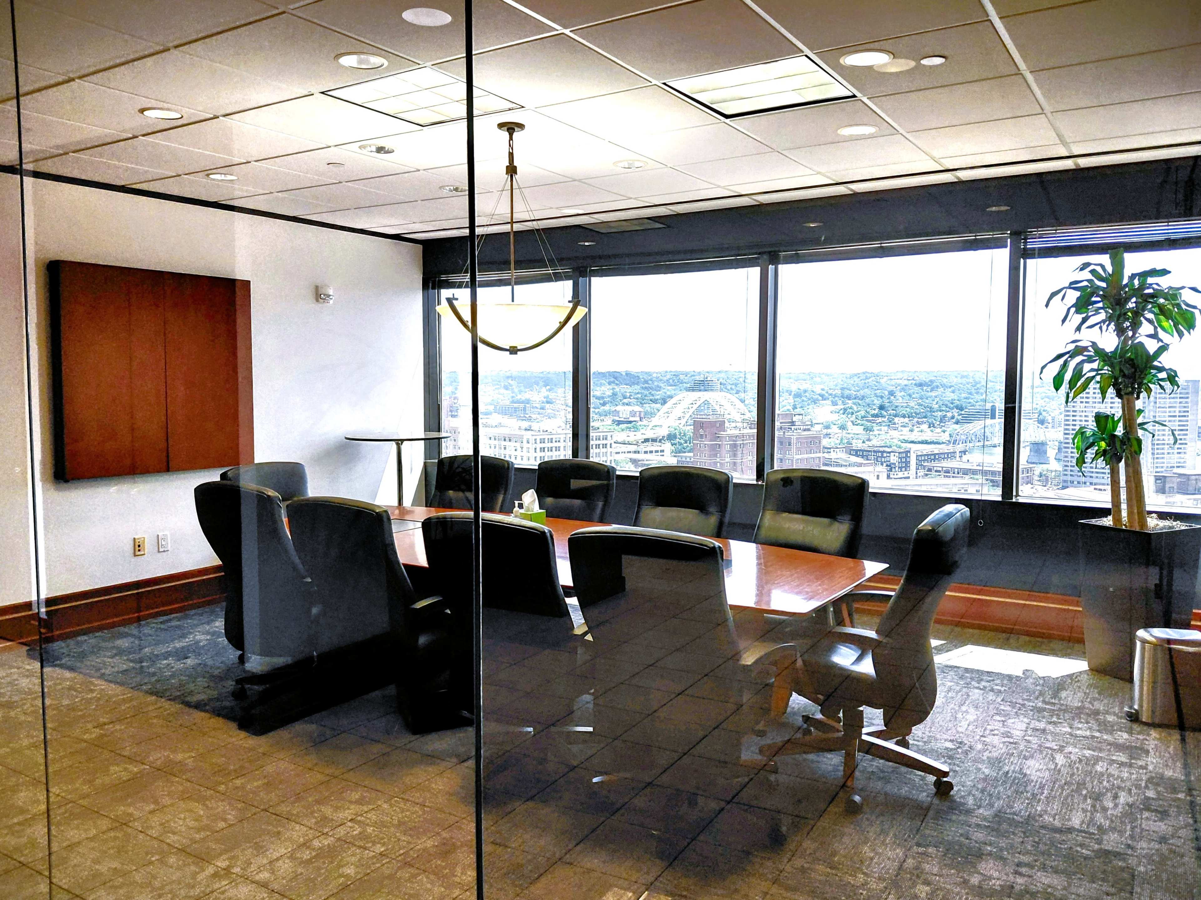 A conference room with a large wooden table and black chairs is visible through a glass wall, offering a view of the city skyline outside.