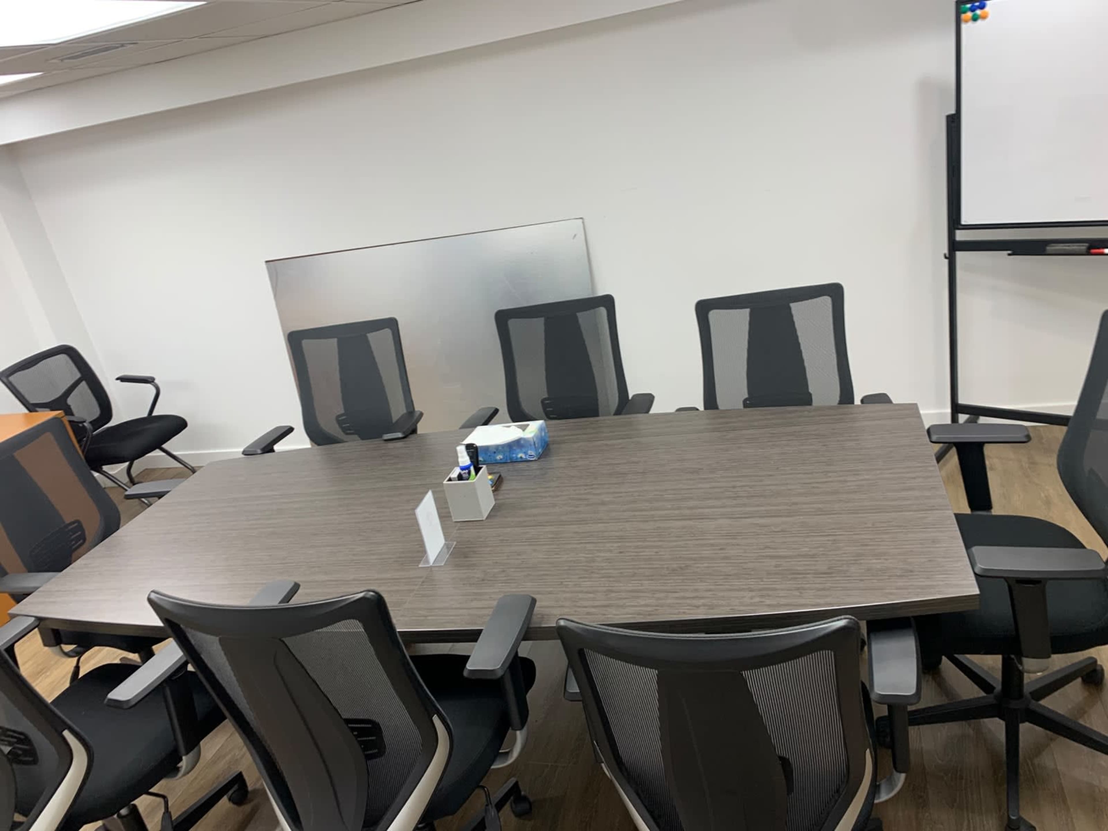The image shows a large conference table surrounded by several ergonomic chairs in a modern office setting.