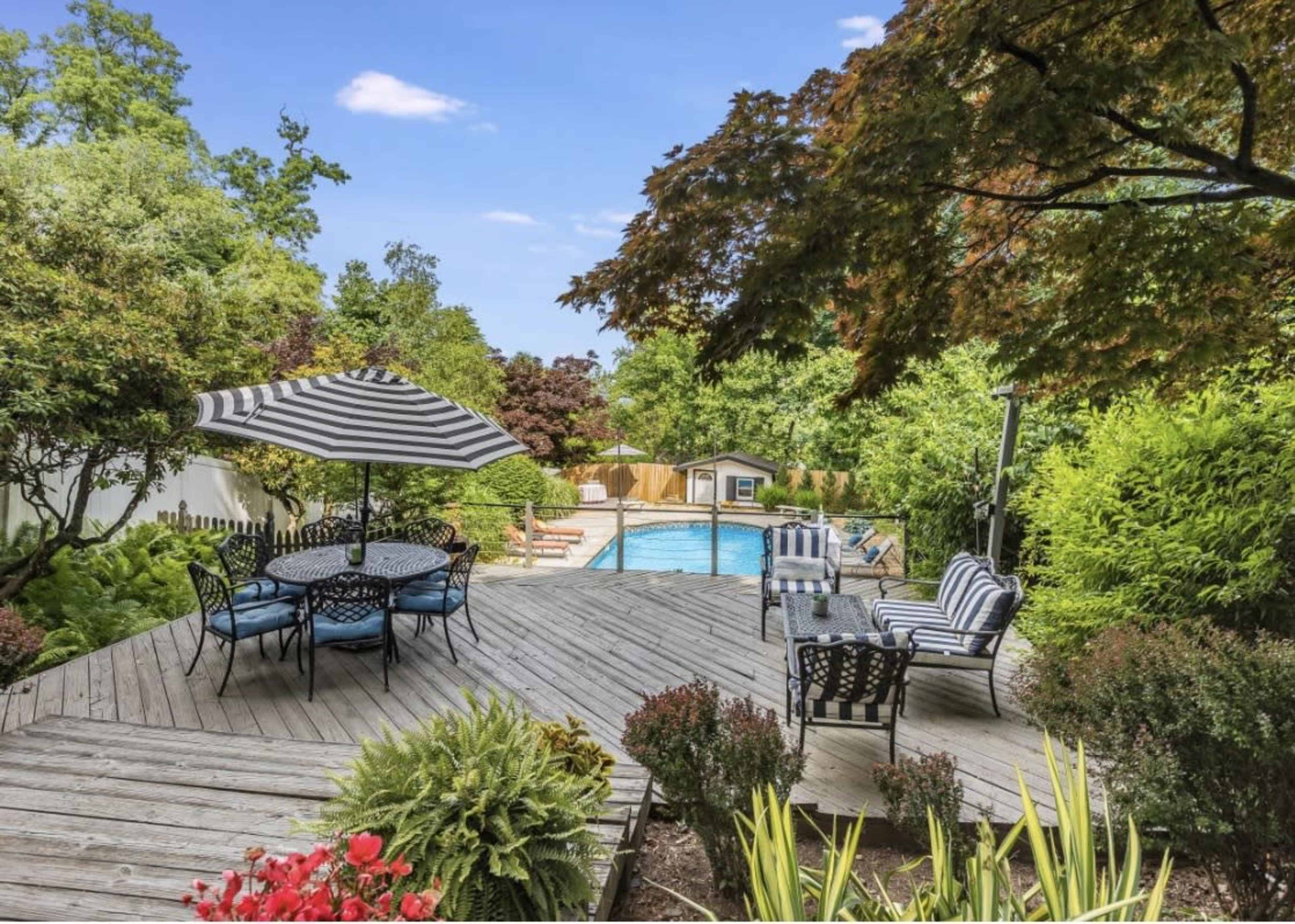 A wooden deck with patterned outdoor furniture overlooks a swimming pool surrounded by lush greenery.