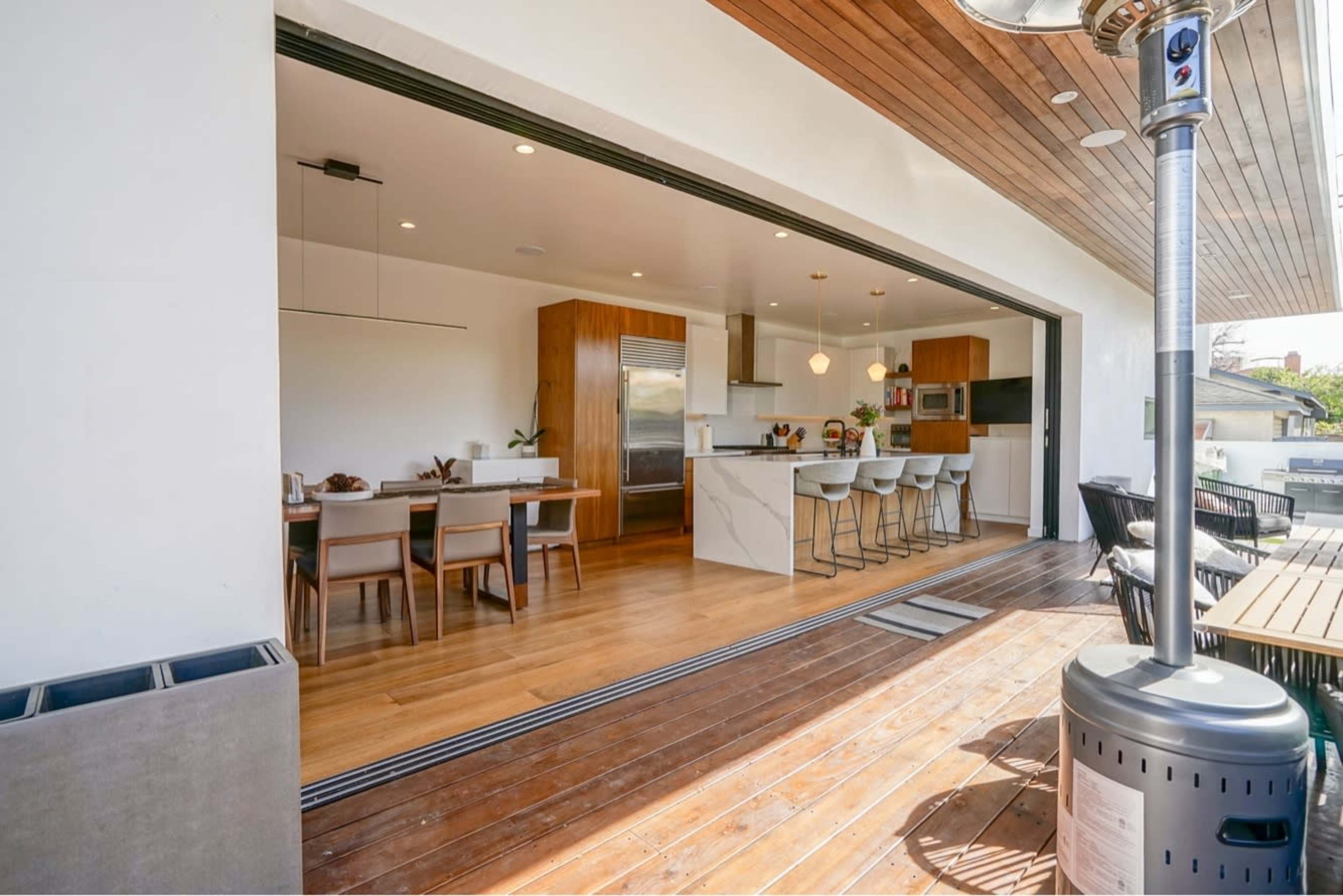 The image shows a modern kitchen and dining area with large sliding doors opening to a wooden deck.