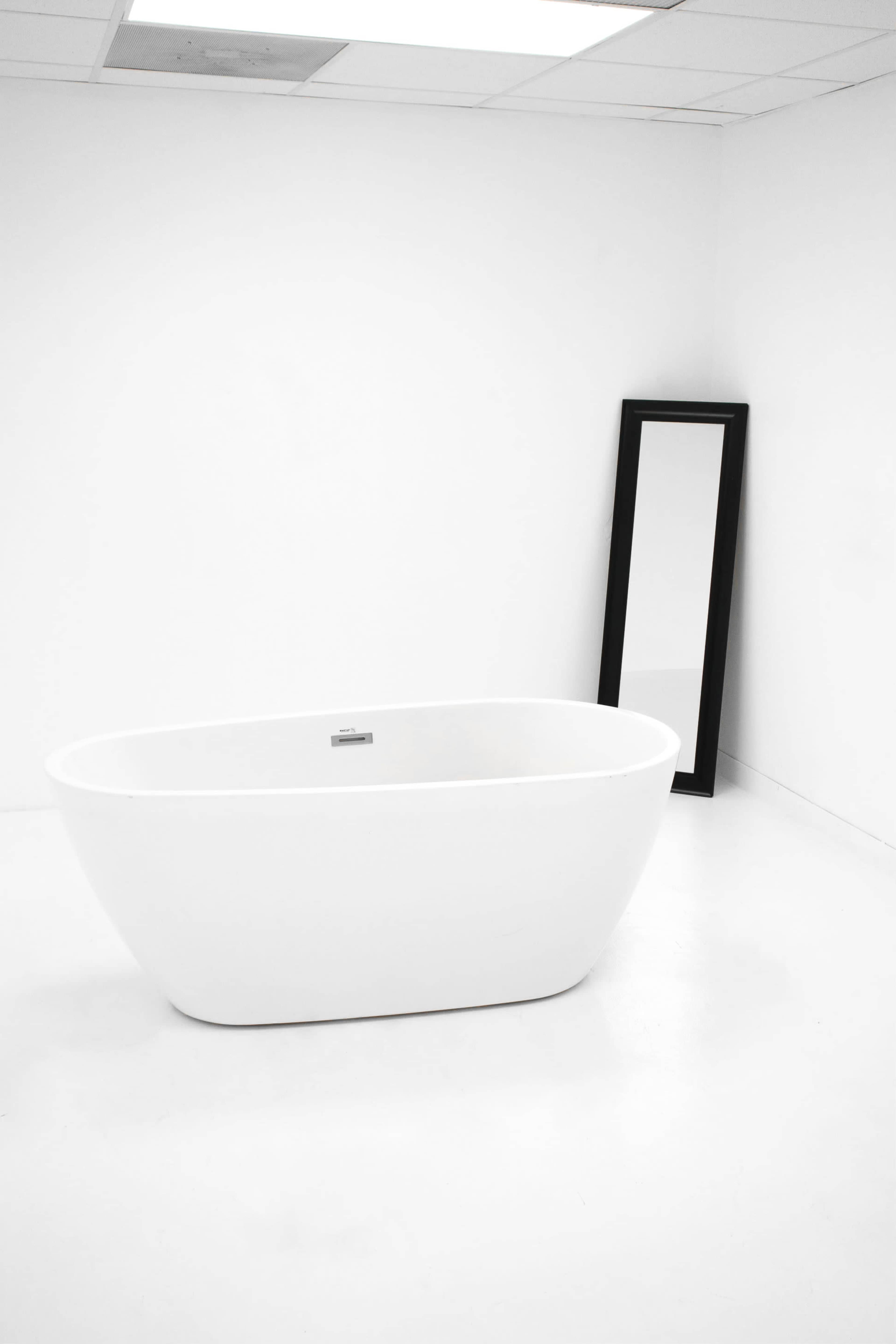 A white freestanding bathtub and a black-framed mirror against a plain white wall in a minimalist room.