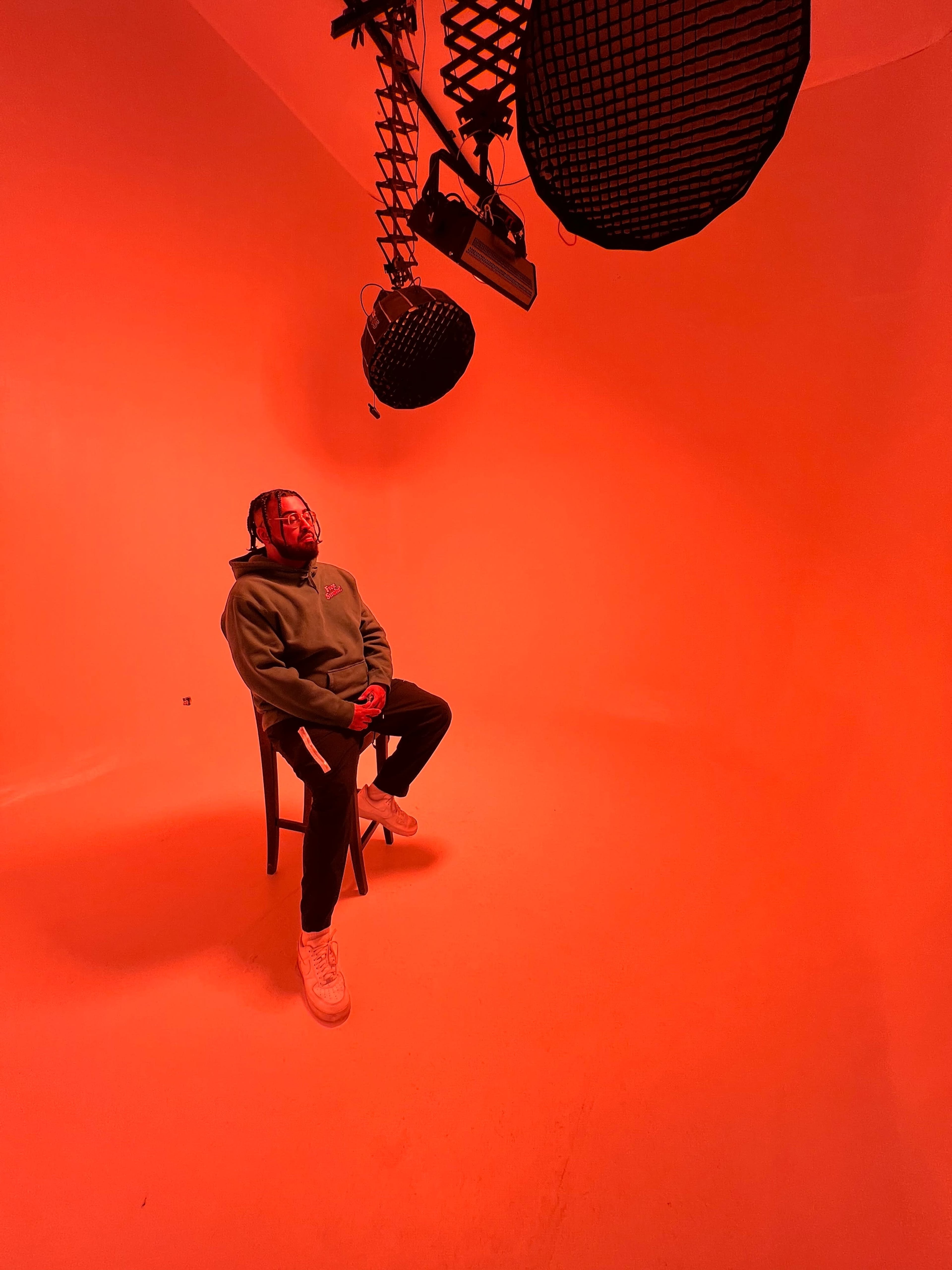 A person sits on a chair in a brightly lit orange studio with overhead lighting fixtures.