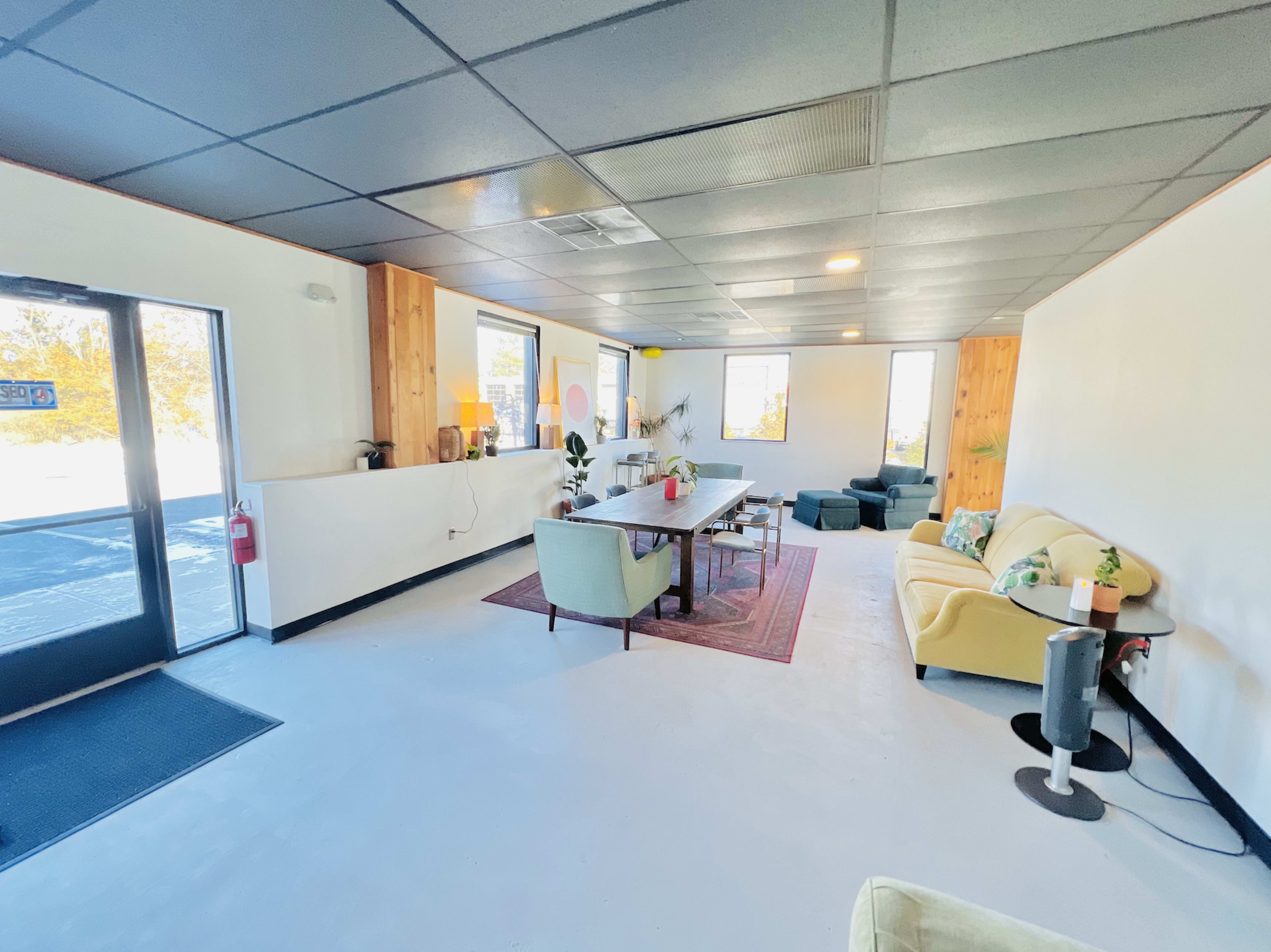 A spacious, modern room with a dining table, various seating options, and large windows allowing natural light to enter.