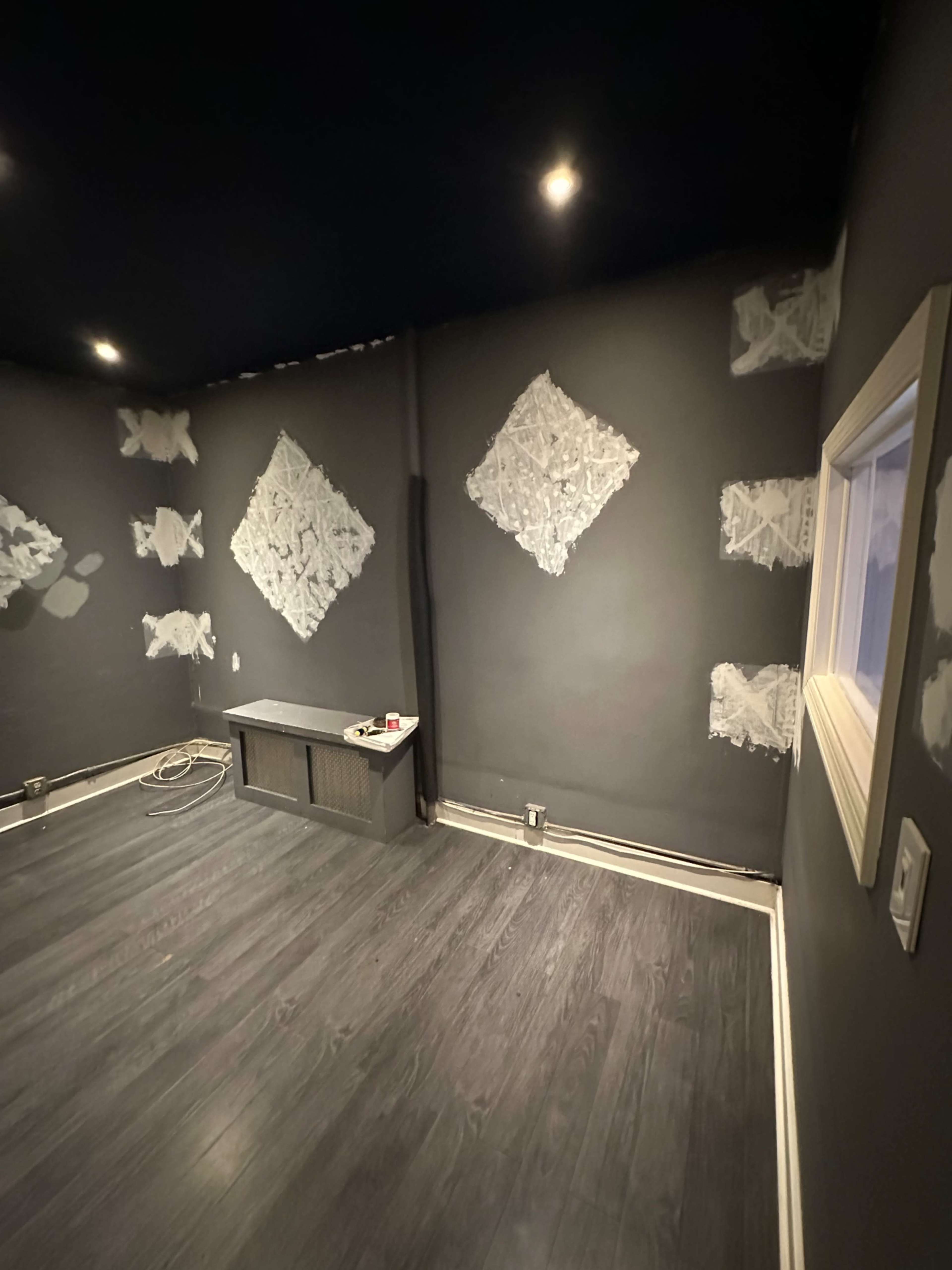 An interior room with dark walls, partially coated with a textured finish, and a wooden floor, featuring a small window and a low cabinet against one wall.