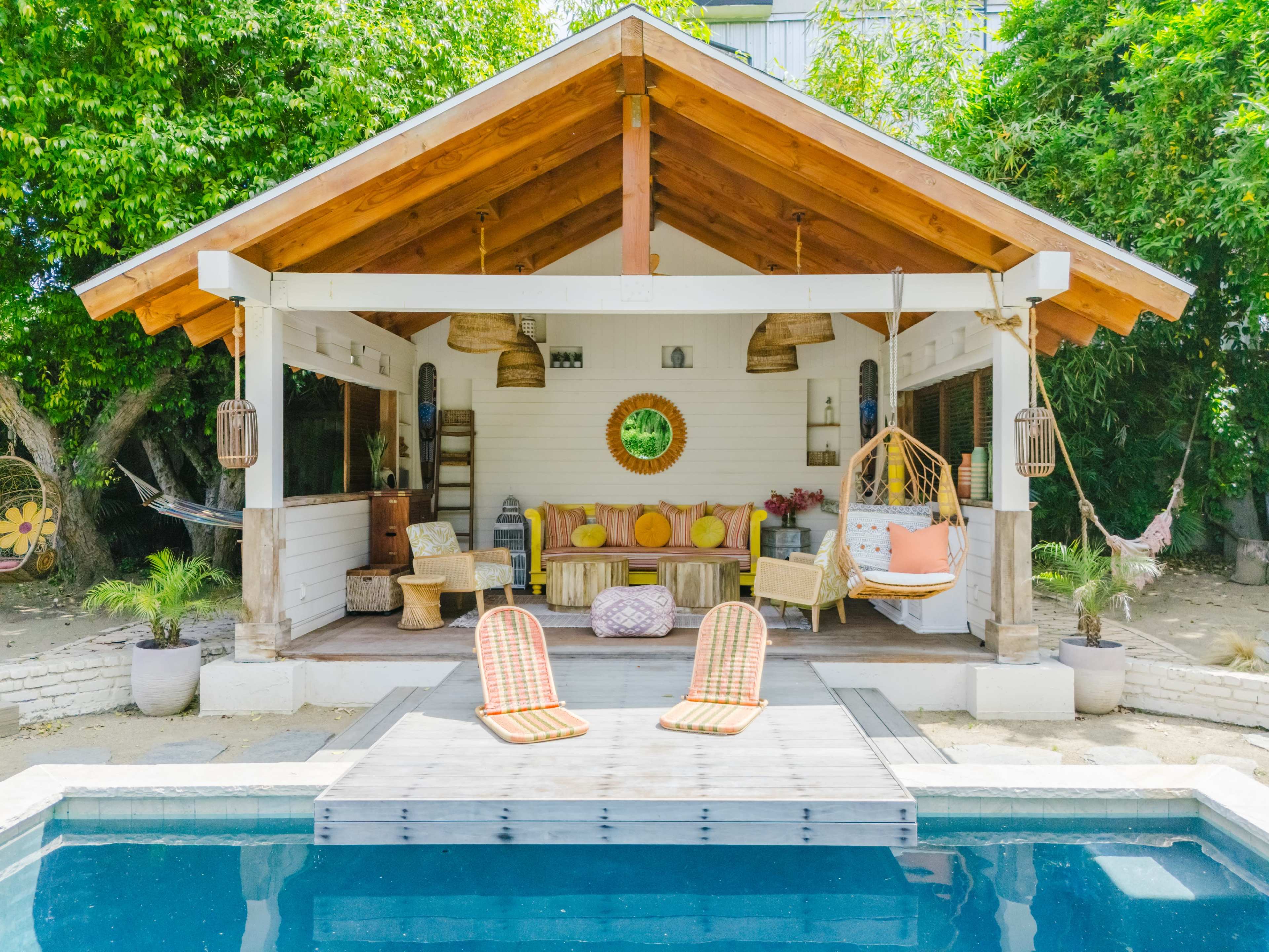 A modern outdoor living area features a covered porch with a seating arrangement and a pool in front.