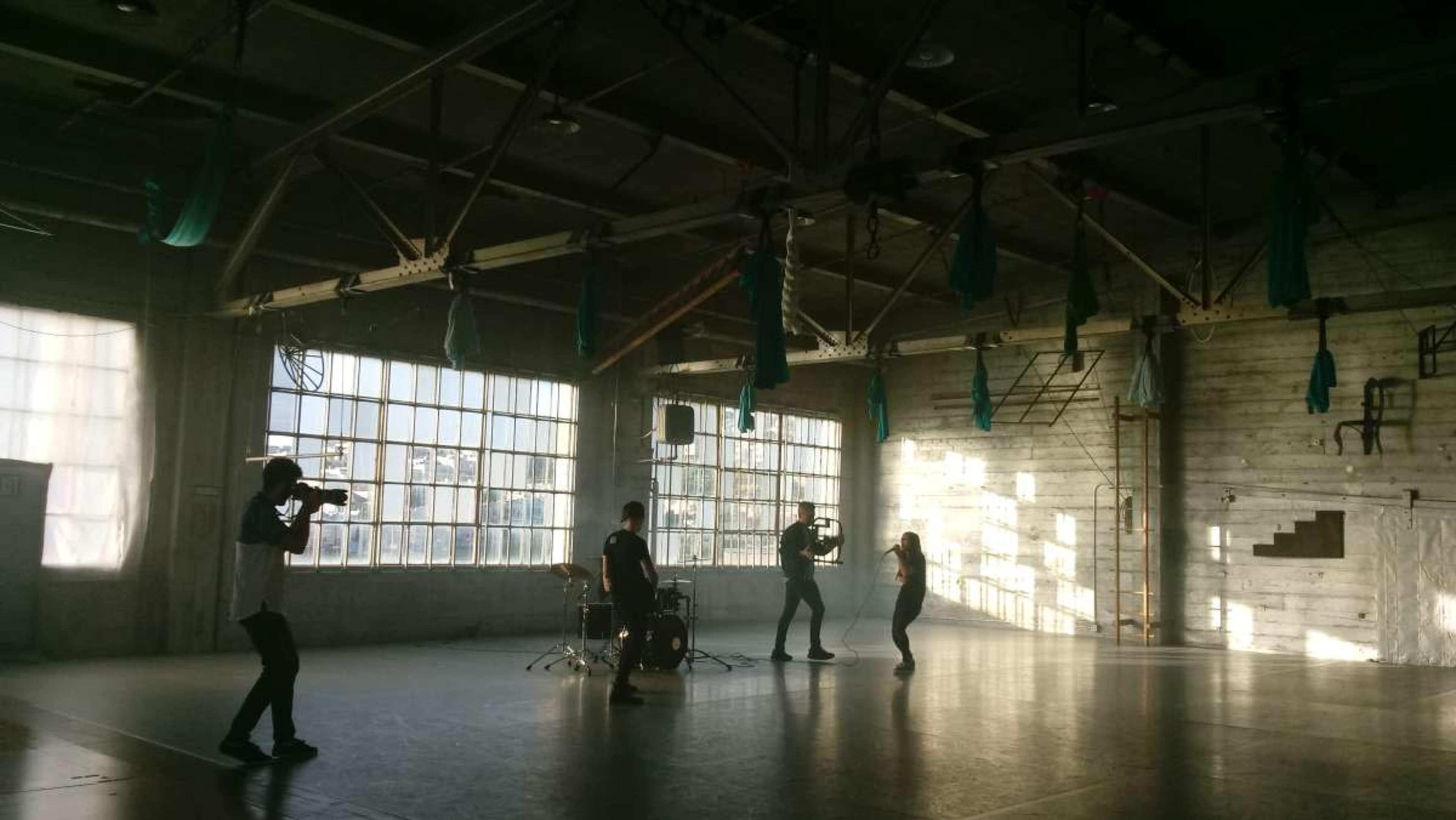 Four individuals are engaged in a photo shoot in an industrial studio with large windows and hanging fabric.