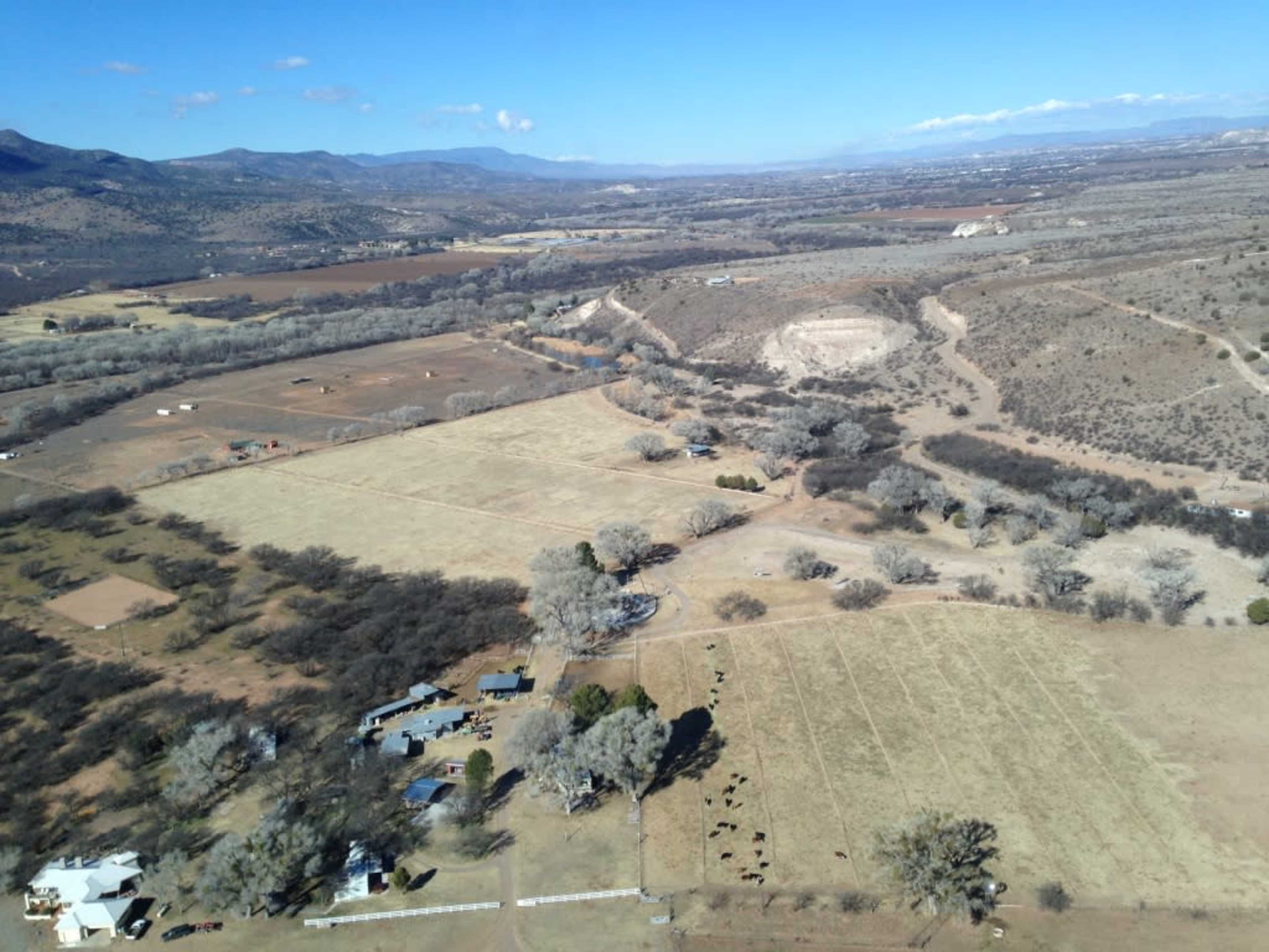 Aerial view of a rural landscape featuring fields, scattered trees, and a small cluster of buildings near livestock.