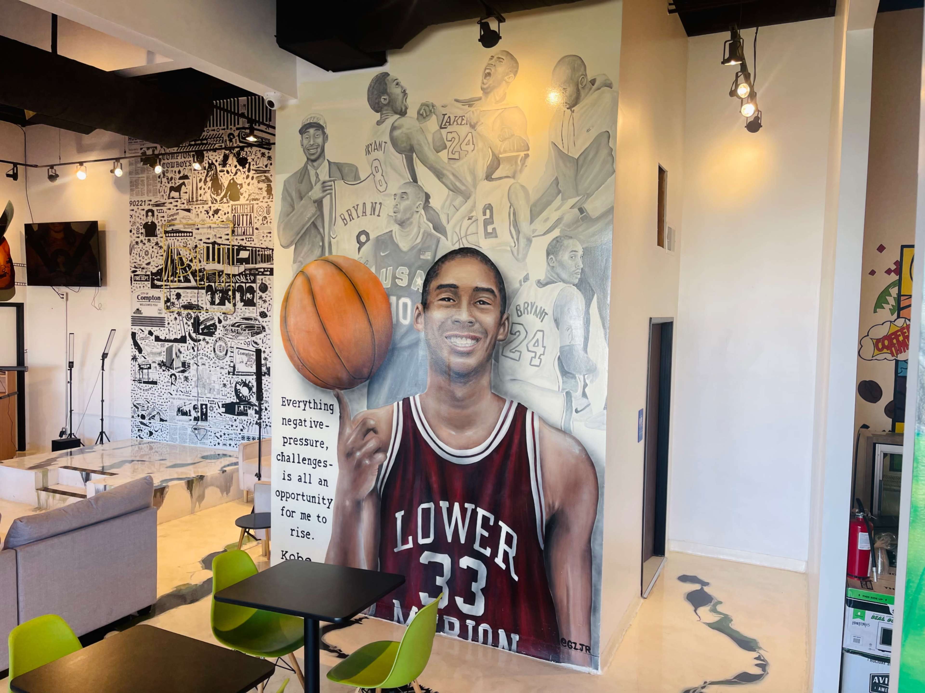 A large mural of a basketball player is painted on a wall in a modern indoor space, featuring inspirational text beneath the image.