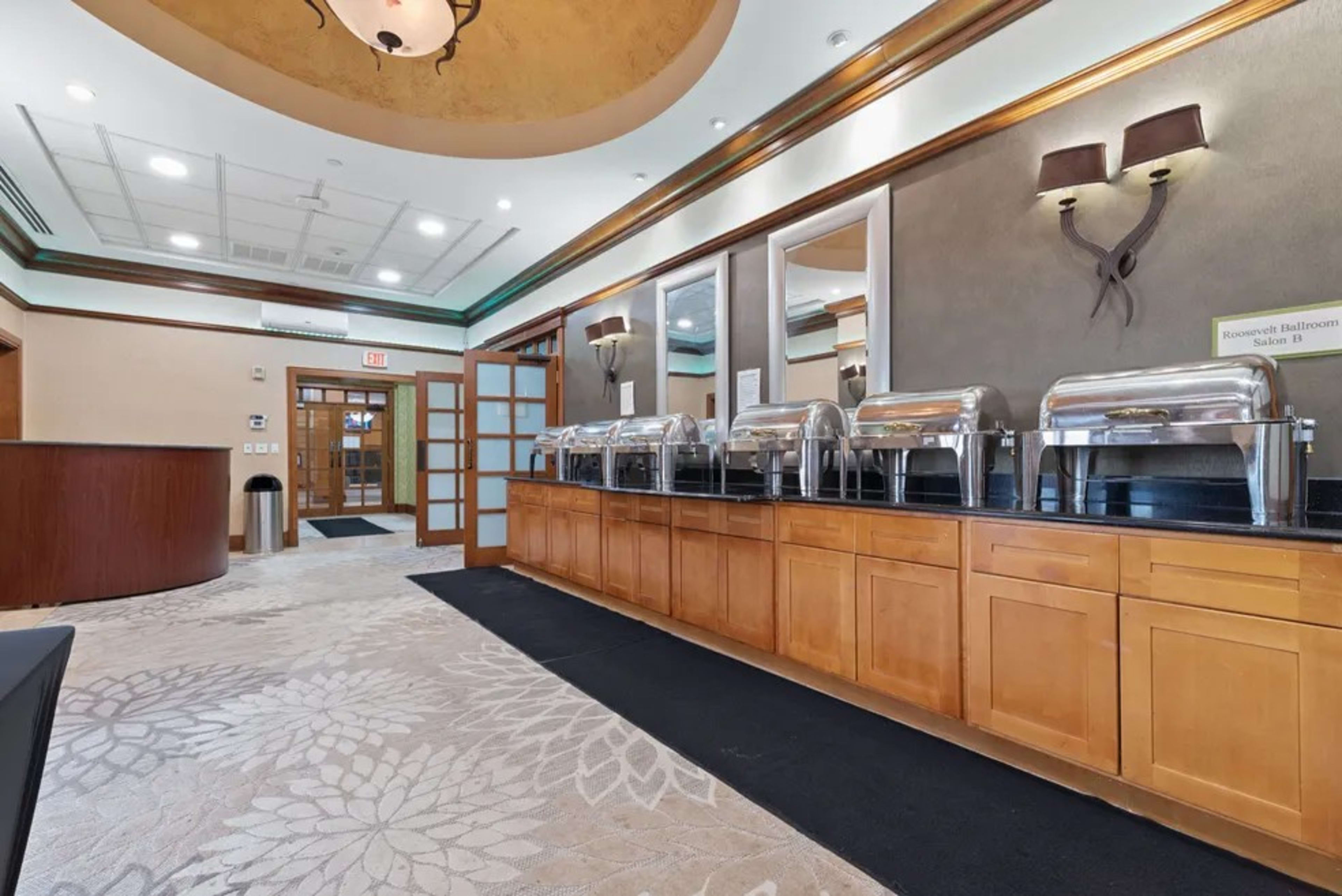 A buffet area with multiple chafing dishes arranged on a countertop in a well-lit room featuring decorative elements on the walls.