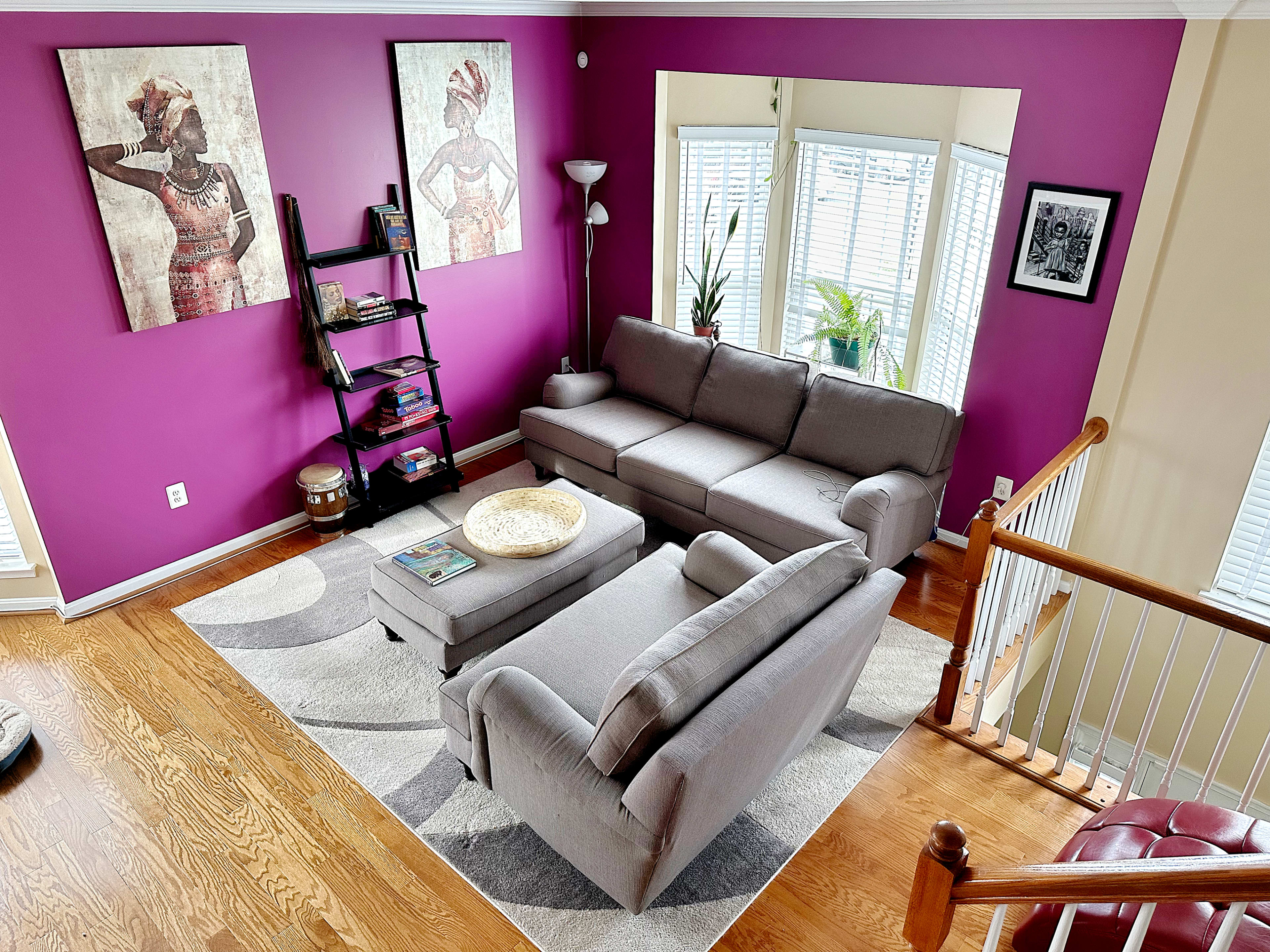 A living room with a gray sectional sofa, a coffee table, a patterned rug, and purple walls adorned with two large framed artworks.