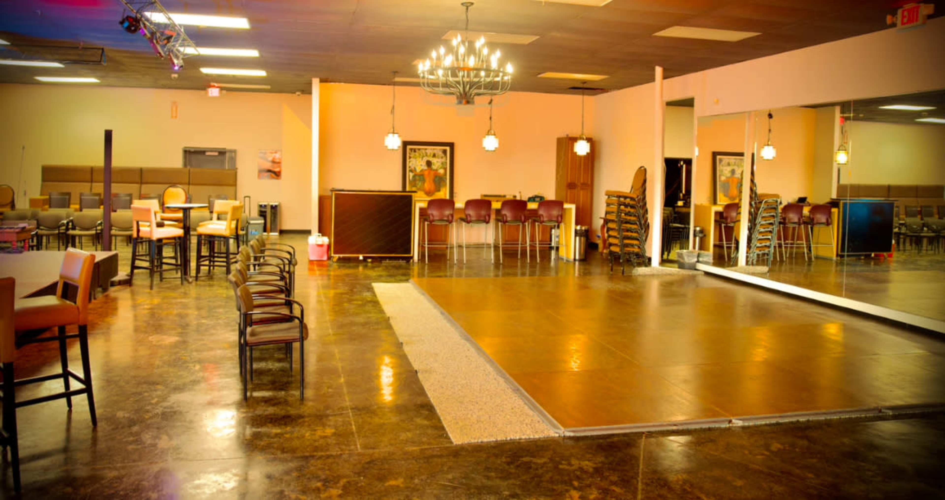The image shows an empty dance hall with polished floors, tables and chairs arranged to the side, and a mirrored wall reflecting the open space.