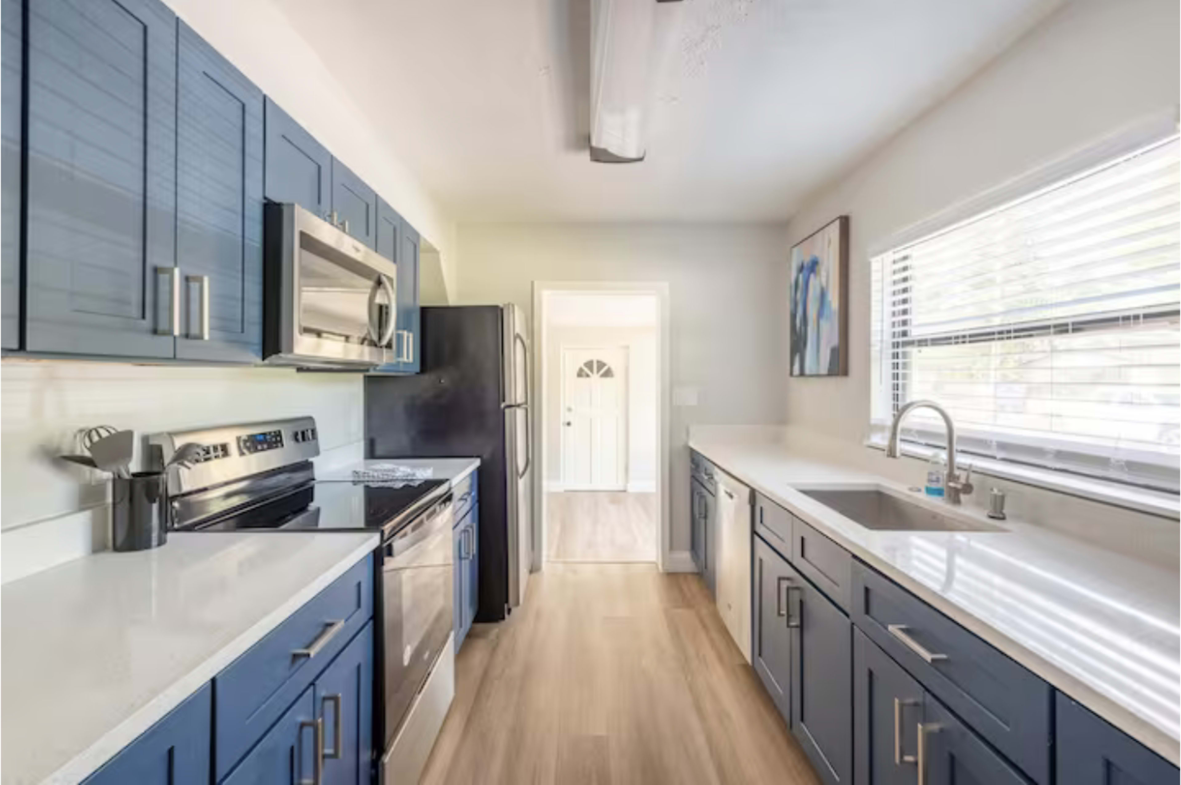 A modern kitchen featuring blue cabinets, stainless steel appliances, and a light-colored countertop with a view toward a door at the end of the room.