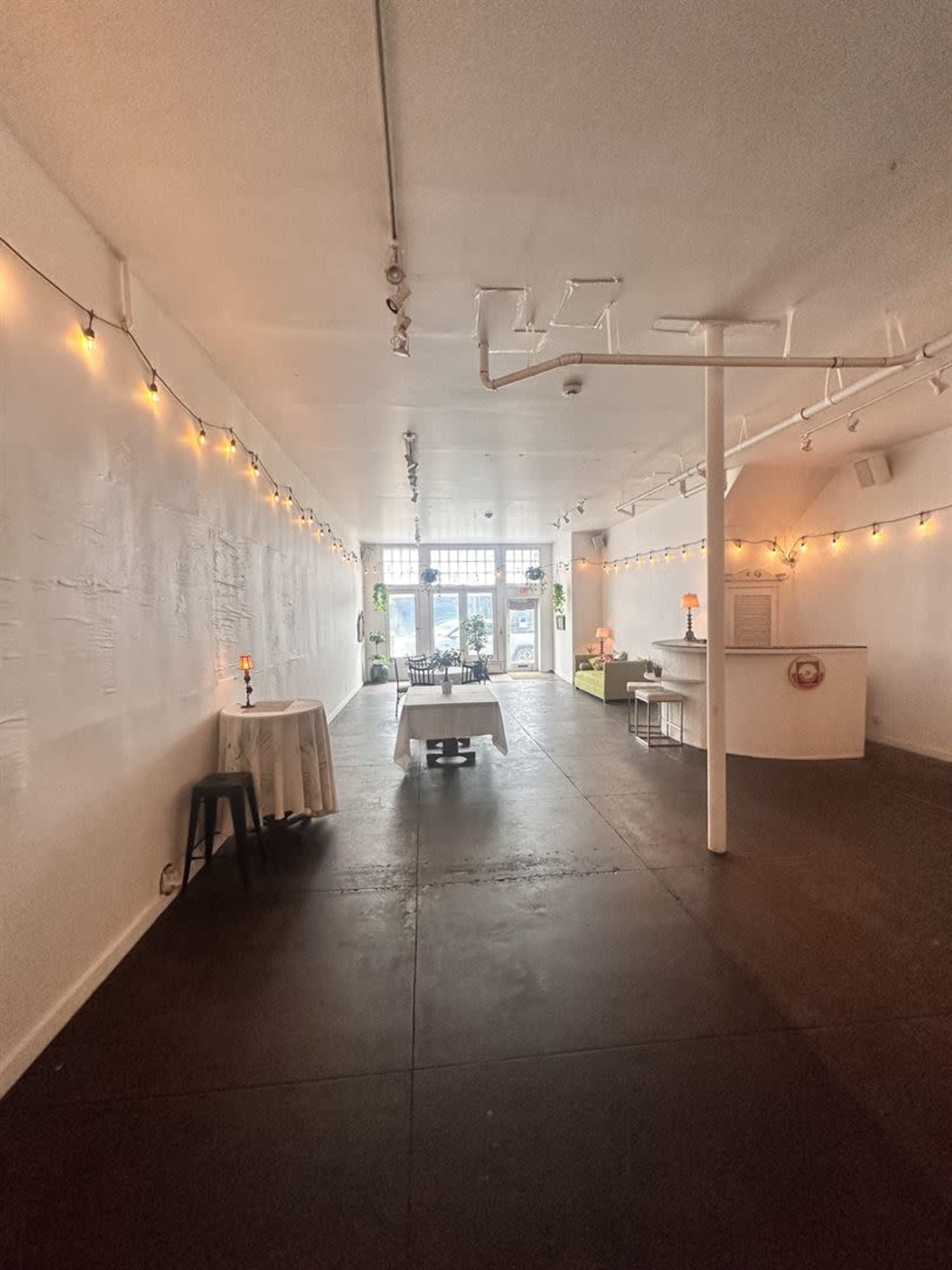 A spacious, well-lit interior of a minimalist venue with tables and decorations, featuring white walls and ambient lighting.
