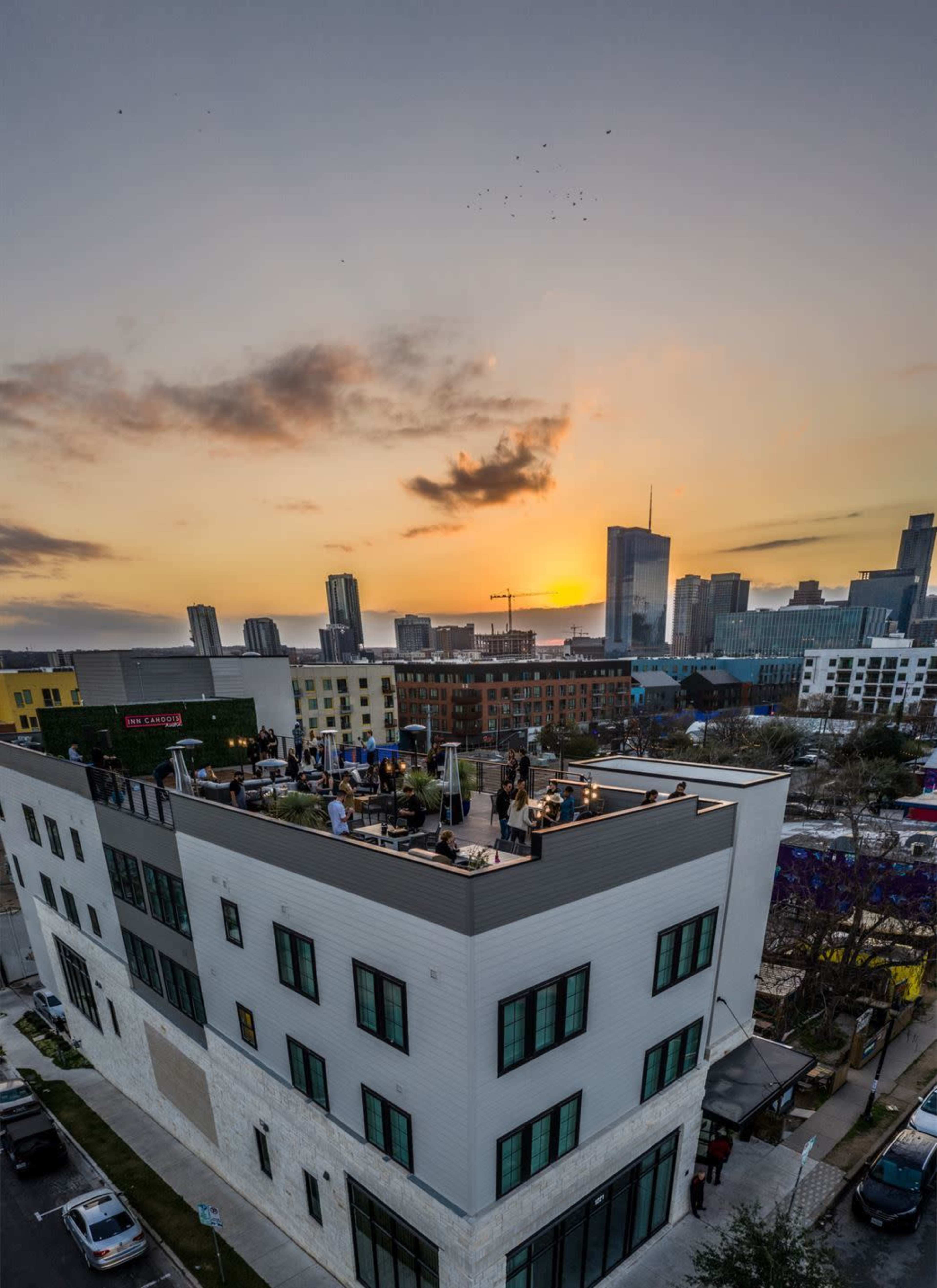 A rooftop view of a building at sunset, with city skyscrapers in the background and people gathered on the roof.