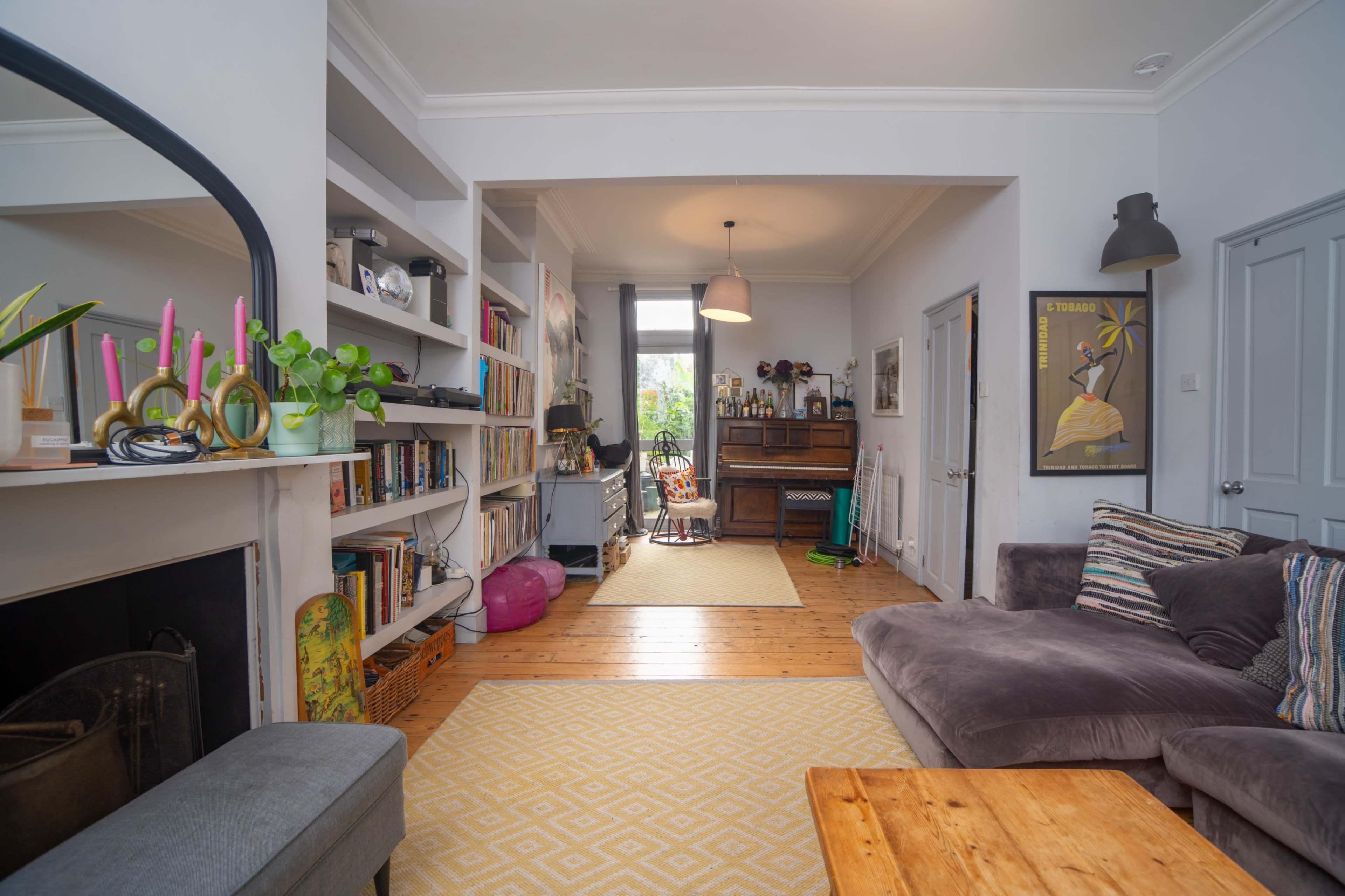 A cozy living room features a gray sofa, wooden coffee table, and shelves filled with books, with a dining area visible in the background.