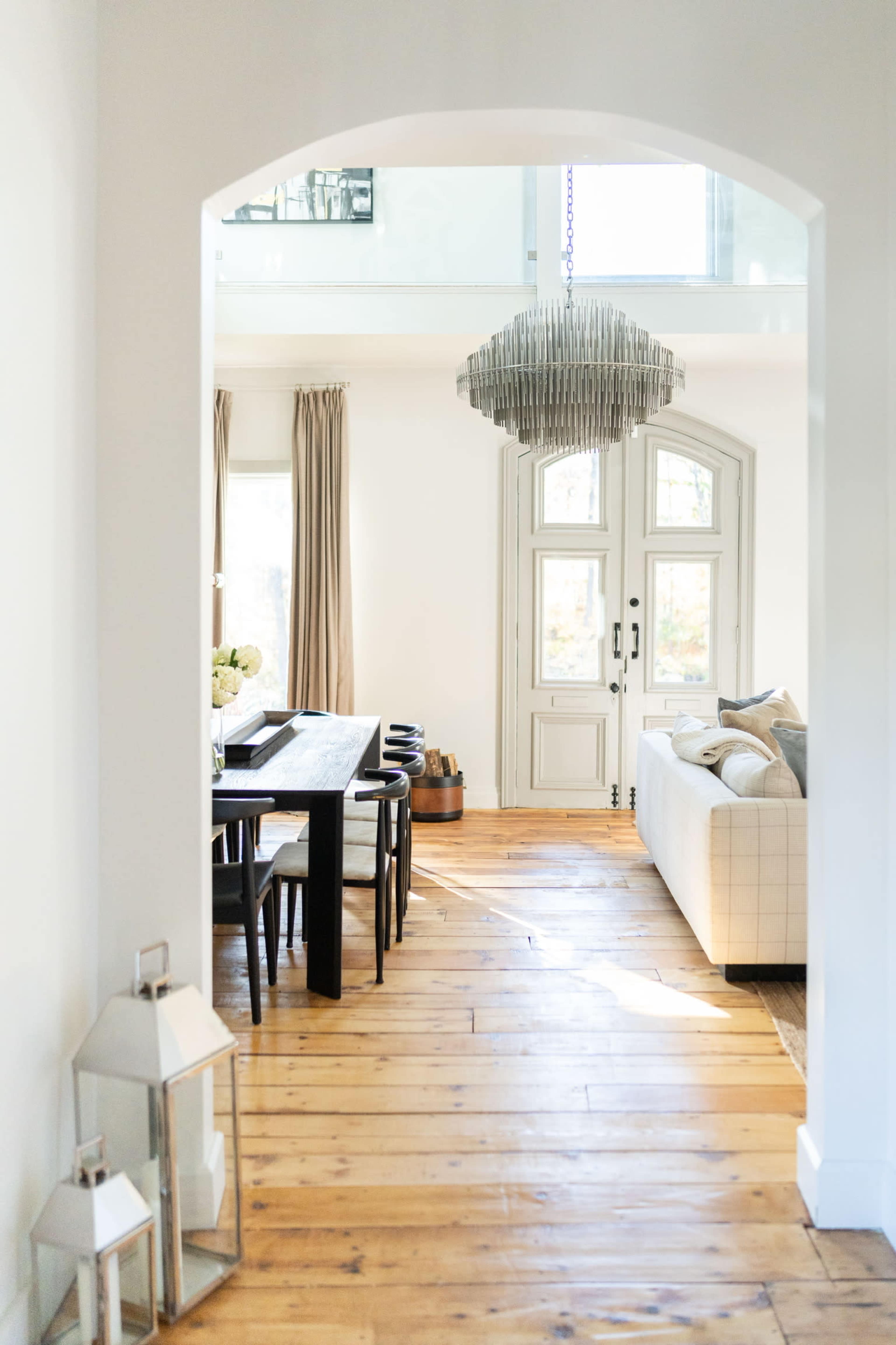 A hallway leads to an open living space featuring a dining table and a sofa, illuminated by natural light from large windows.