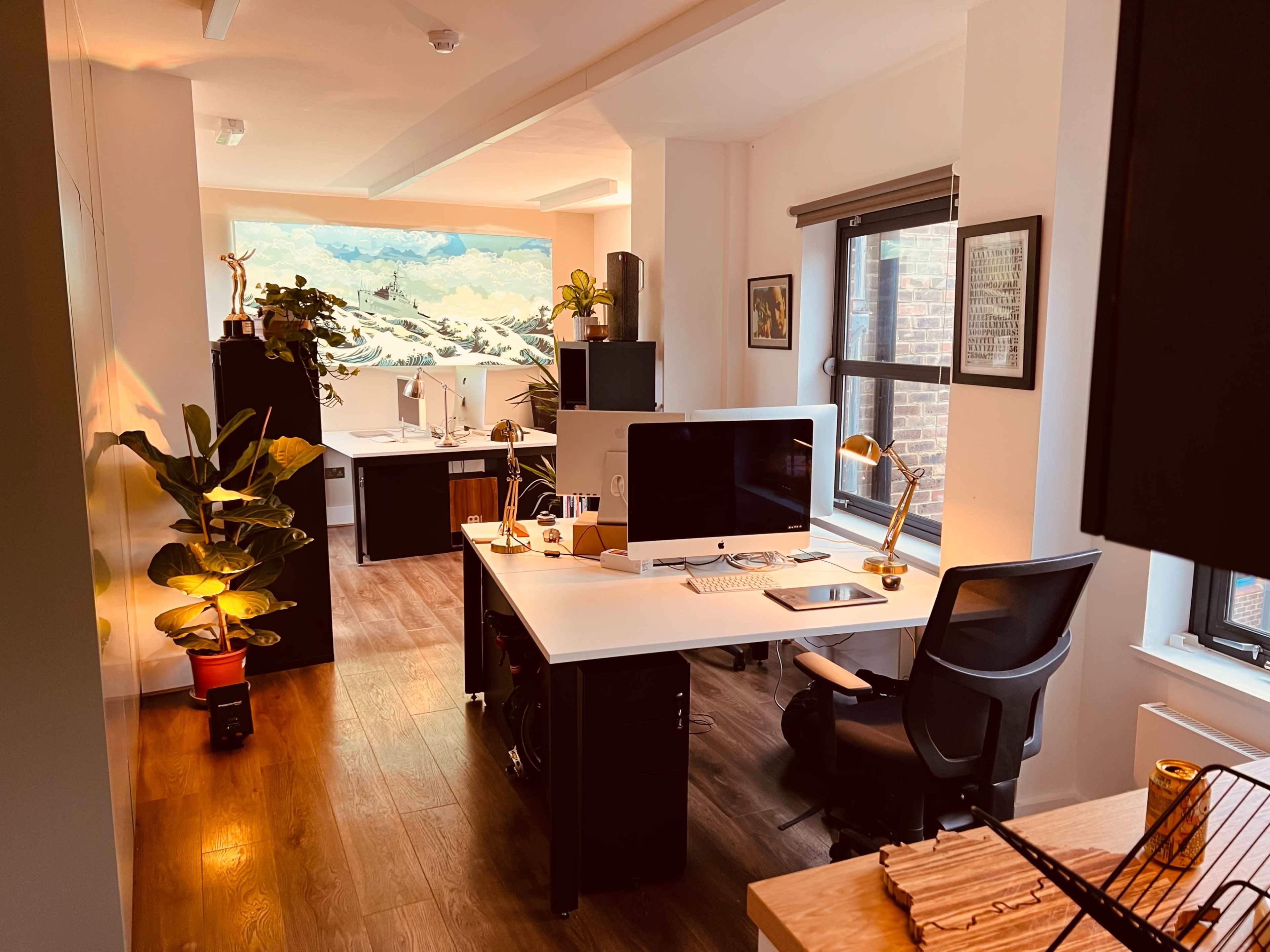 A modern office space with two workstations, featuring desks with computers, plants, and artwork on the walls.