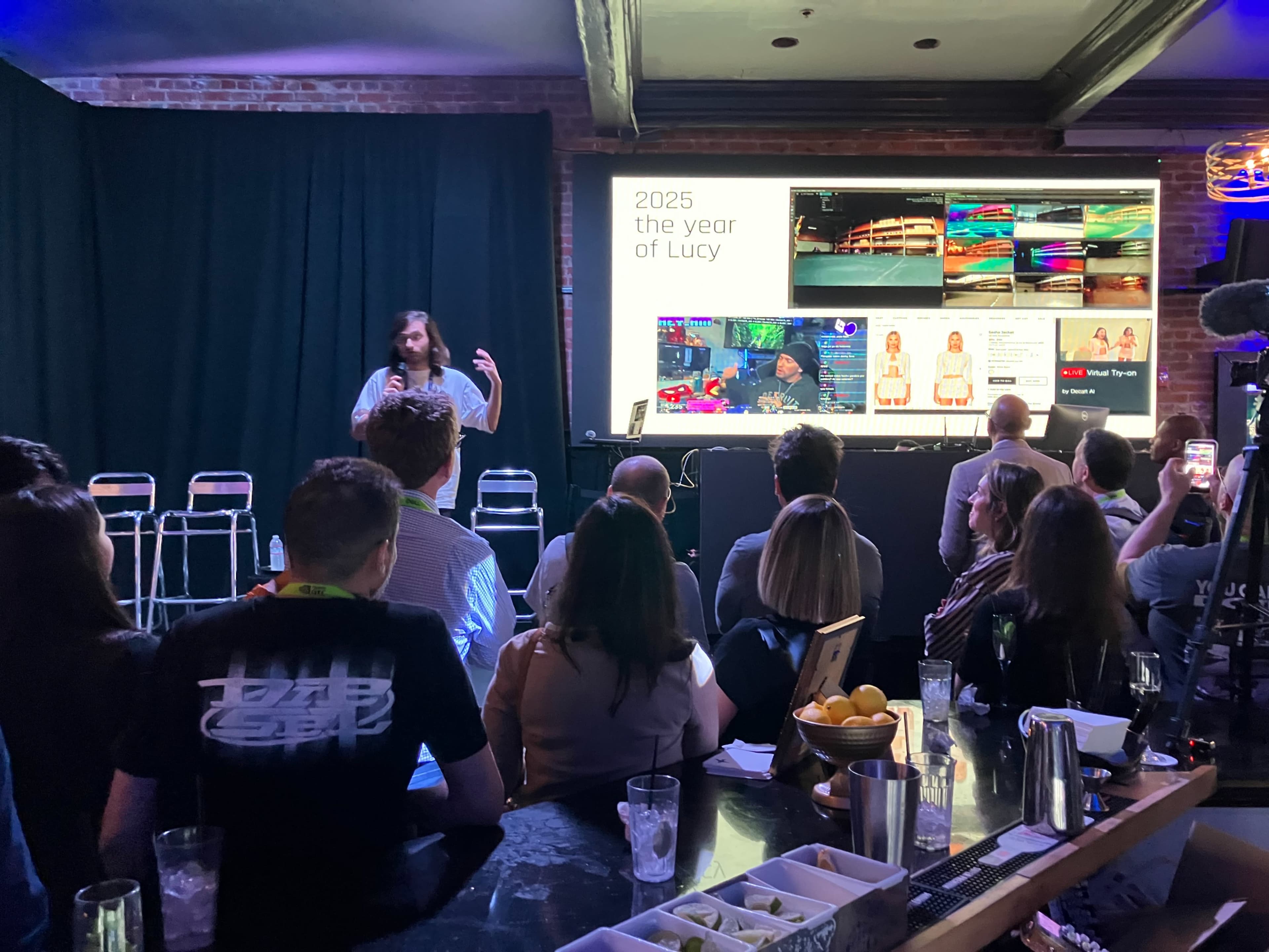A speaker presents information about "2025 the year of Lucy" to an audience seated at a bar.
