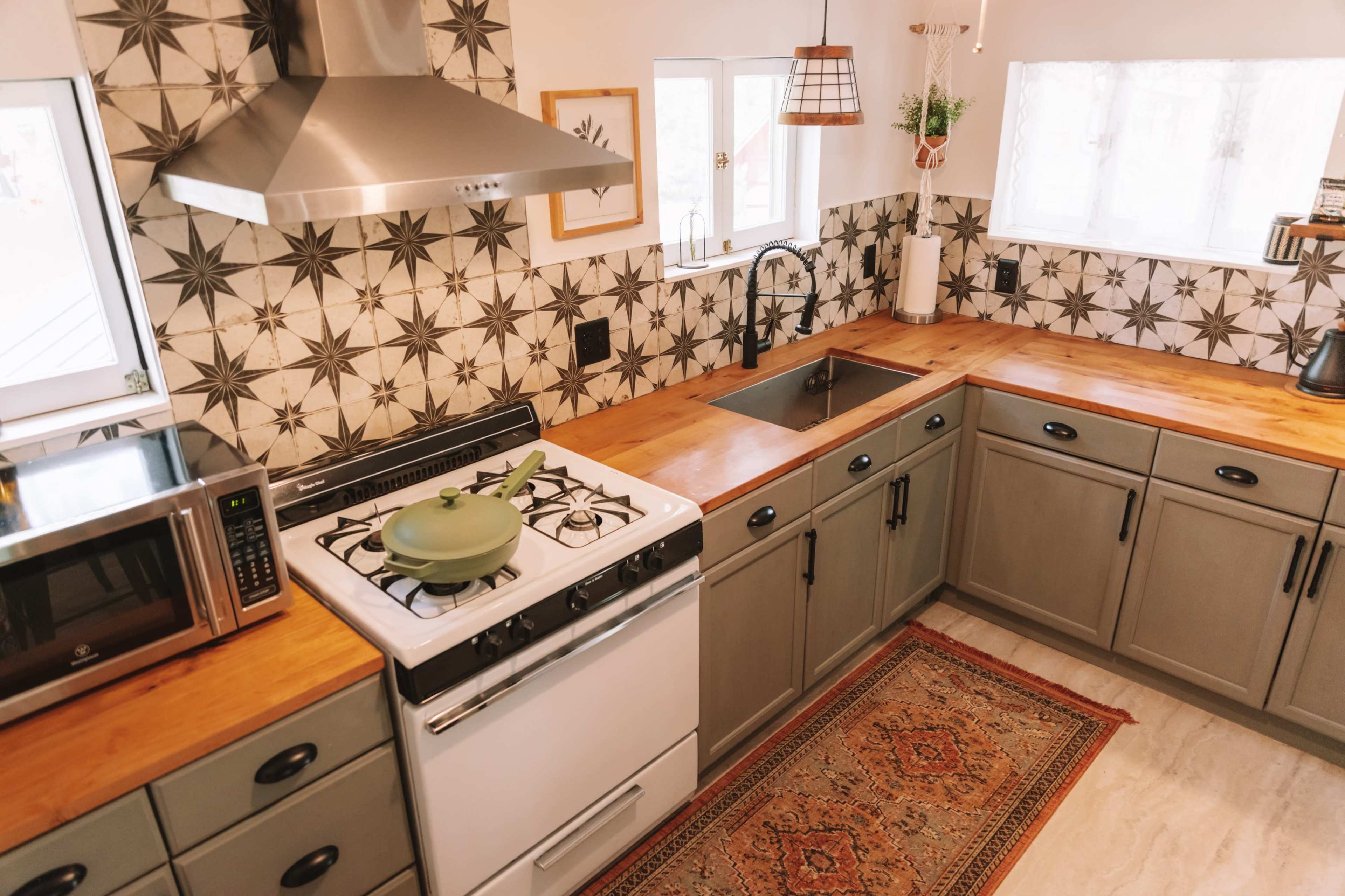 The image shows a modern kitchen with a gas stove, a stainless steel hood, wooden countertops, and patterned tiles on the walls.