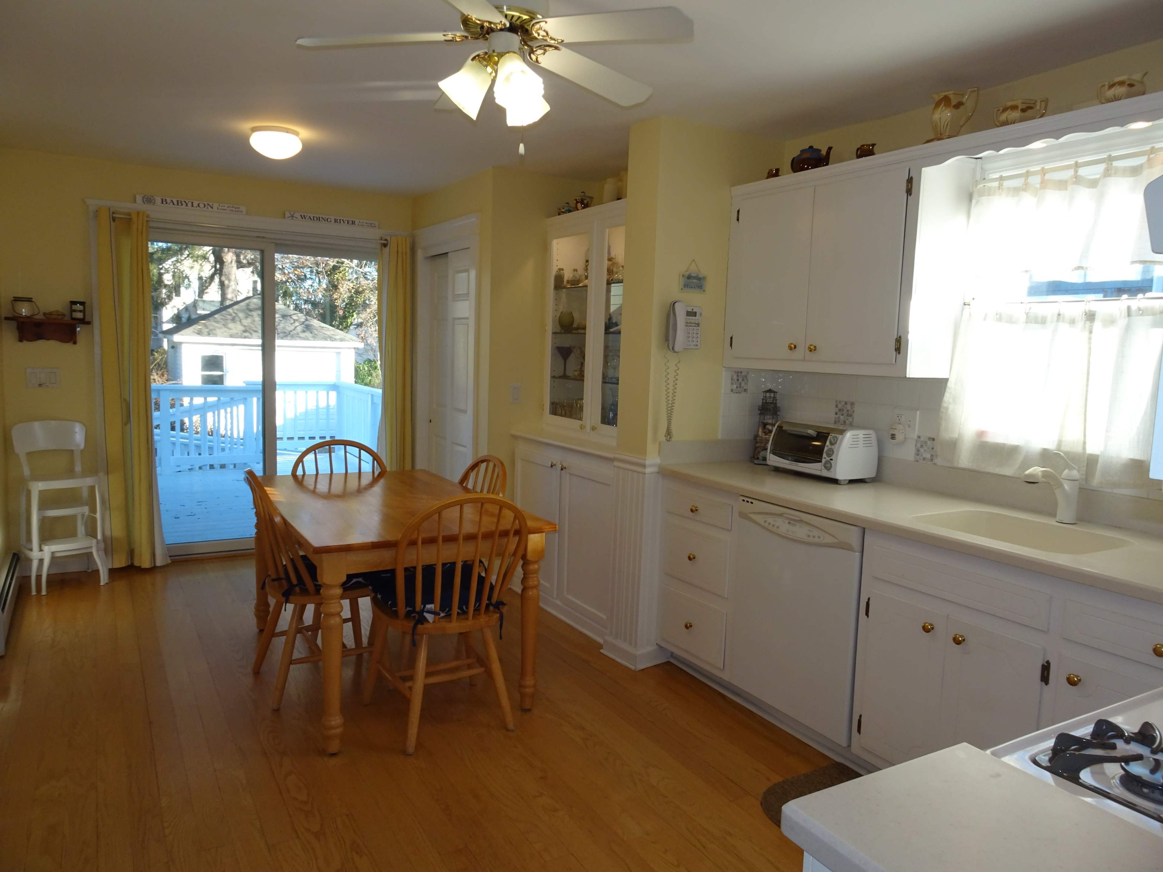 A bright kitchen with a wooden table and chairs, white cabinets, and a sliding glass door leading to a deck.