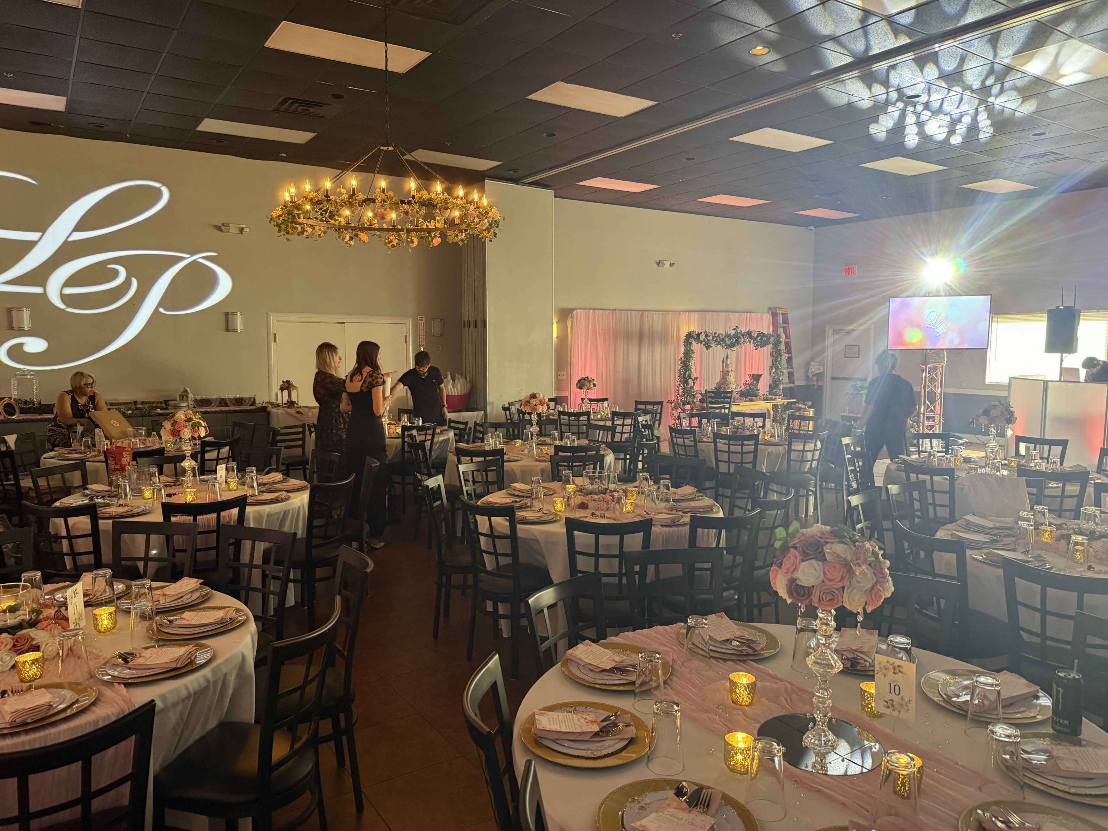 The image shows a banquet hall set up for an event, featuring elegantly arranged tables with floral centerpieces and soft lighting.