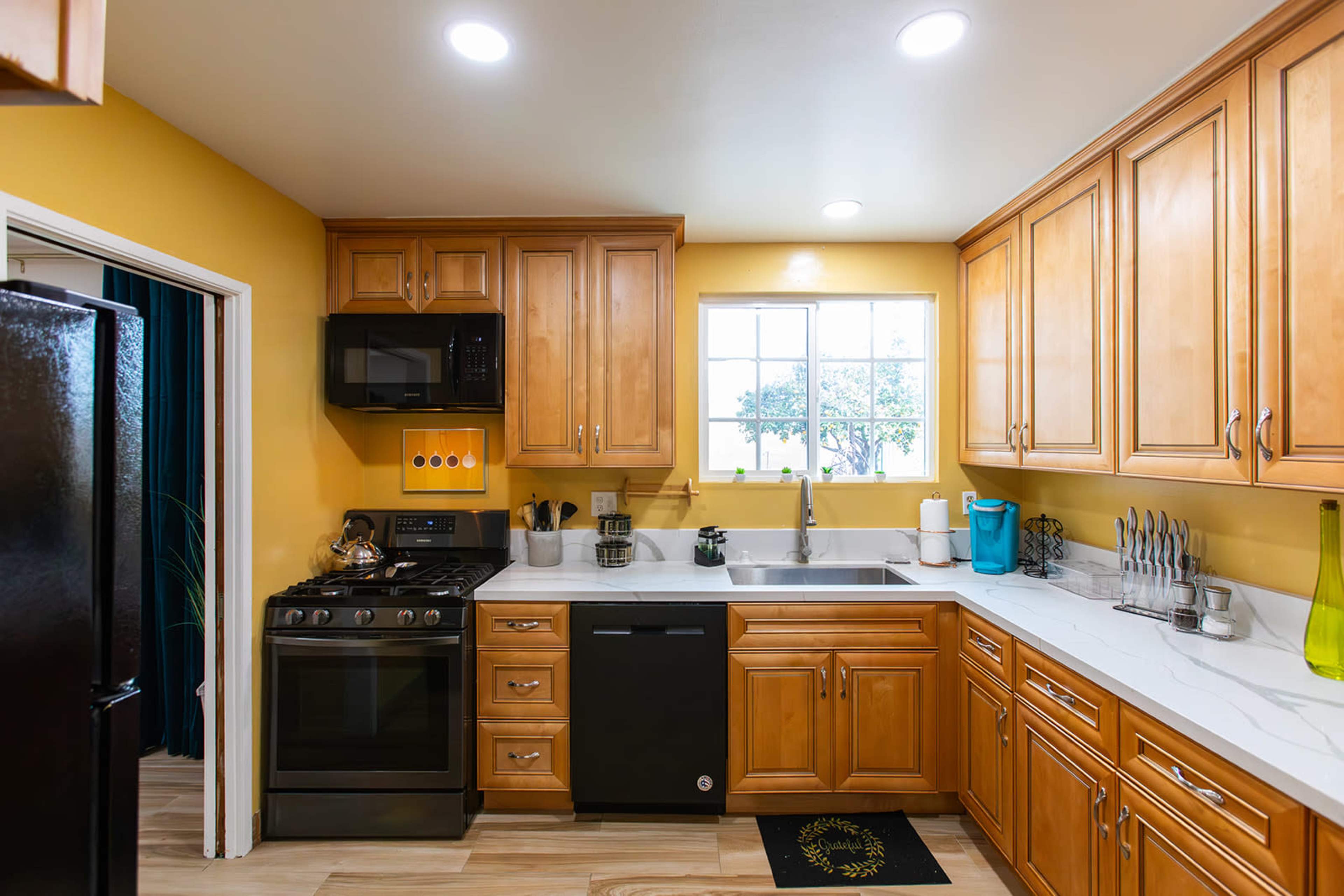 A kitchen featuring wooden cabinets, a black stove, a black dishwasher, and a large window above the sink.