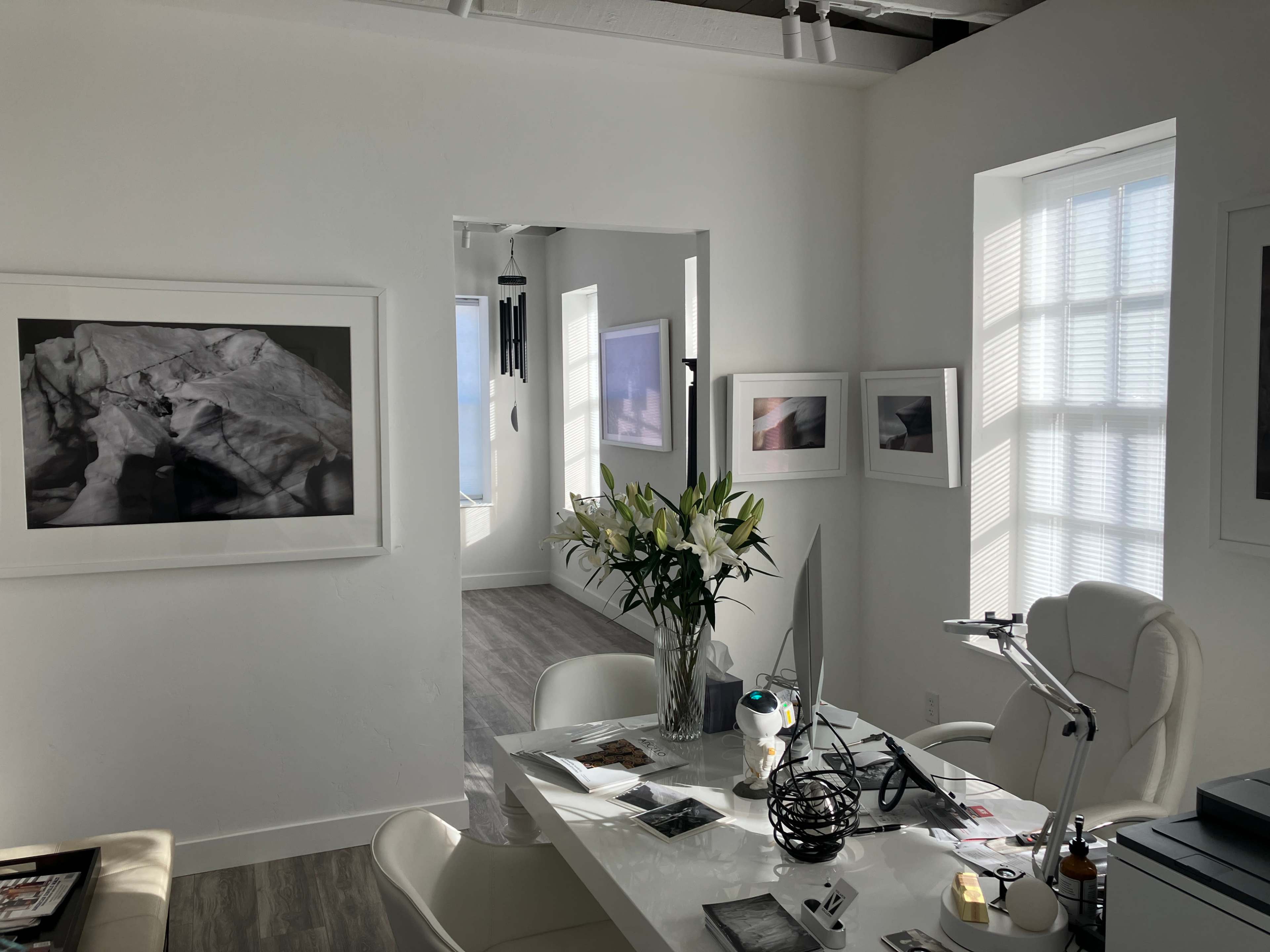 A bright, modern office with a large desk, white furnishings, and framed black-and-white photographs on the walls.