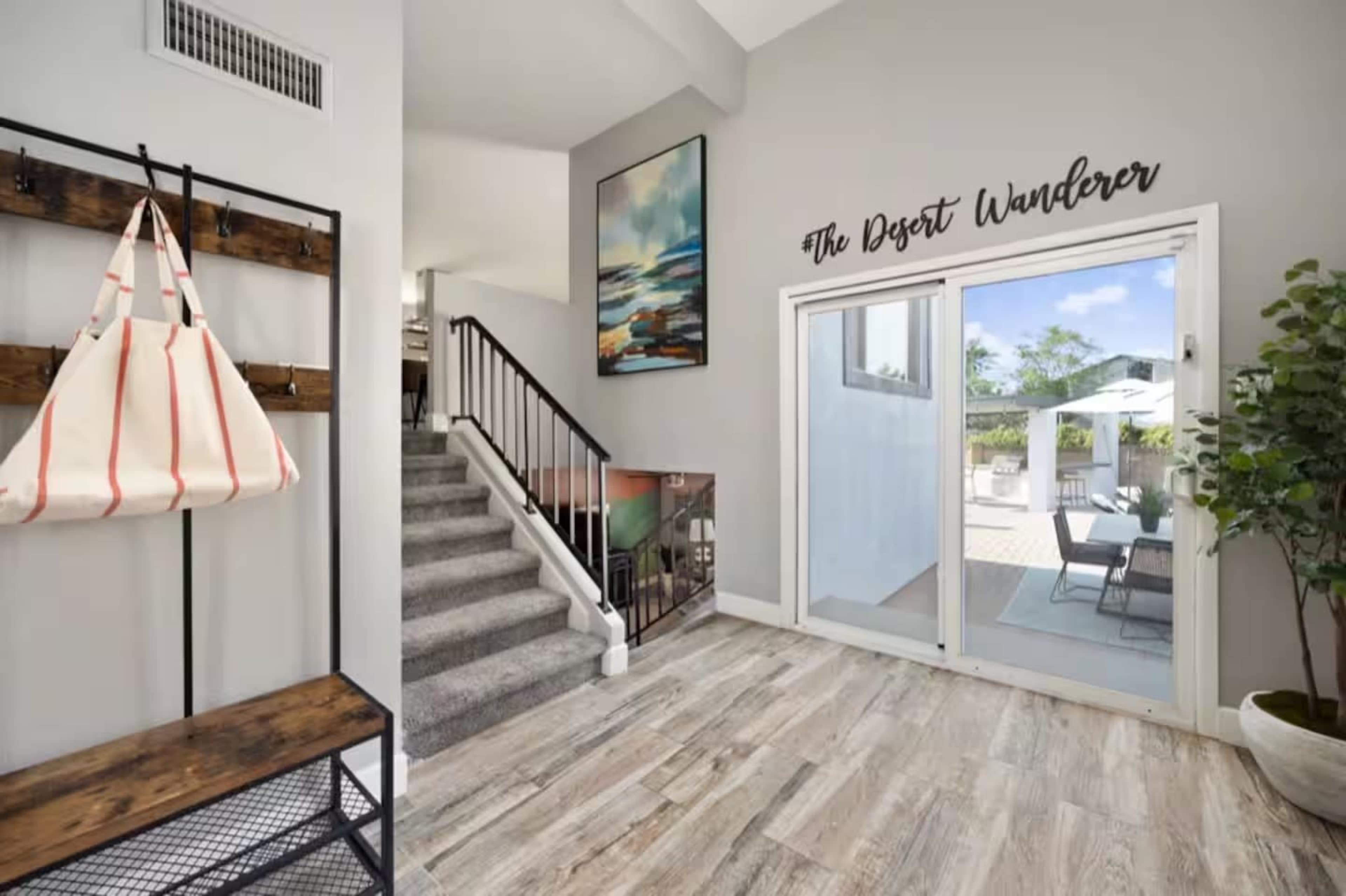 The image shows an entrance area with a coat rack, stairs leading to the upper level, and a sliding glass door that opens to a patio area.