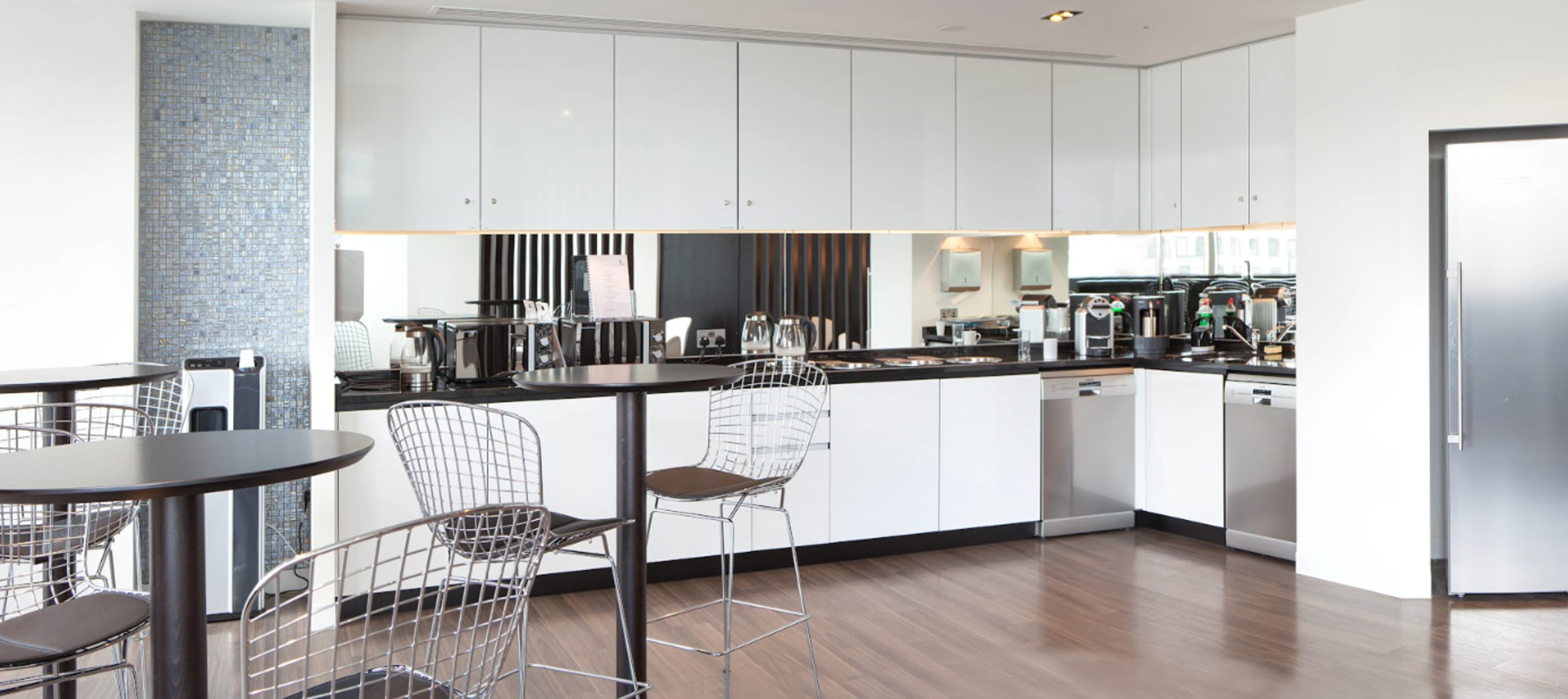 A modern kitchen with white cabinetry, stainless steel appliances, and bar seating at two tall tables.