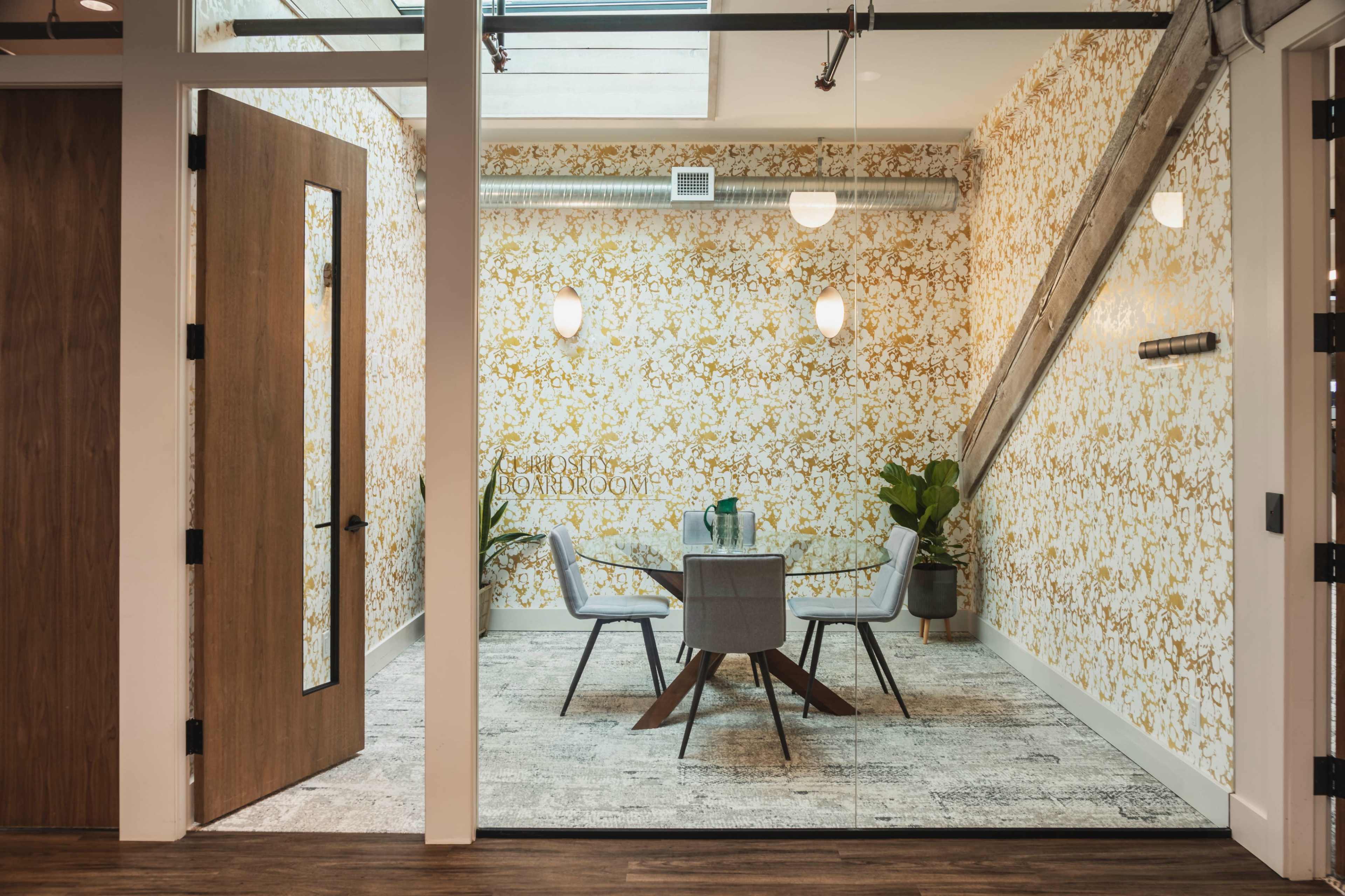 The image shows a modern meeting room featuring a round table surrounded by four chairs, with decorative wallpaper and a large window.