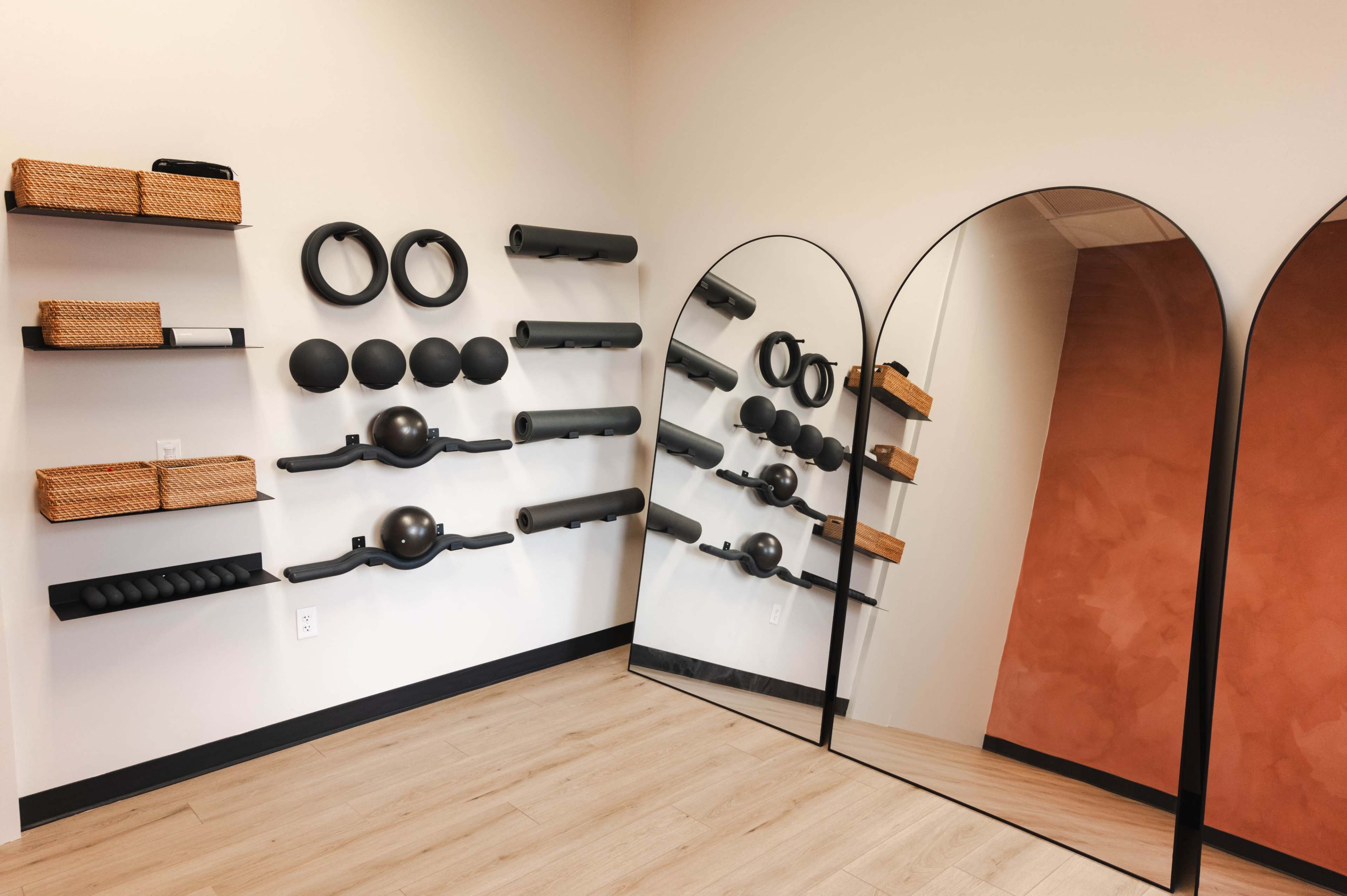 The image shows a fitness space with black exercise equipment mounted on the wall, two large mirrors, and wooden flooring.