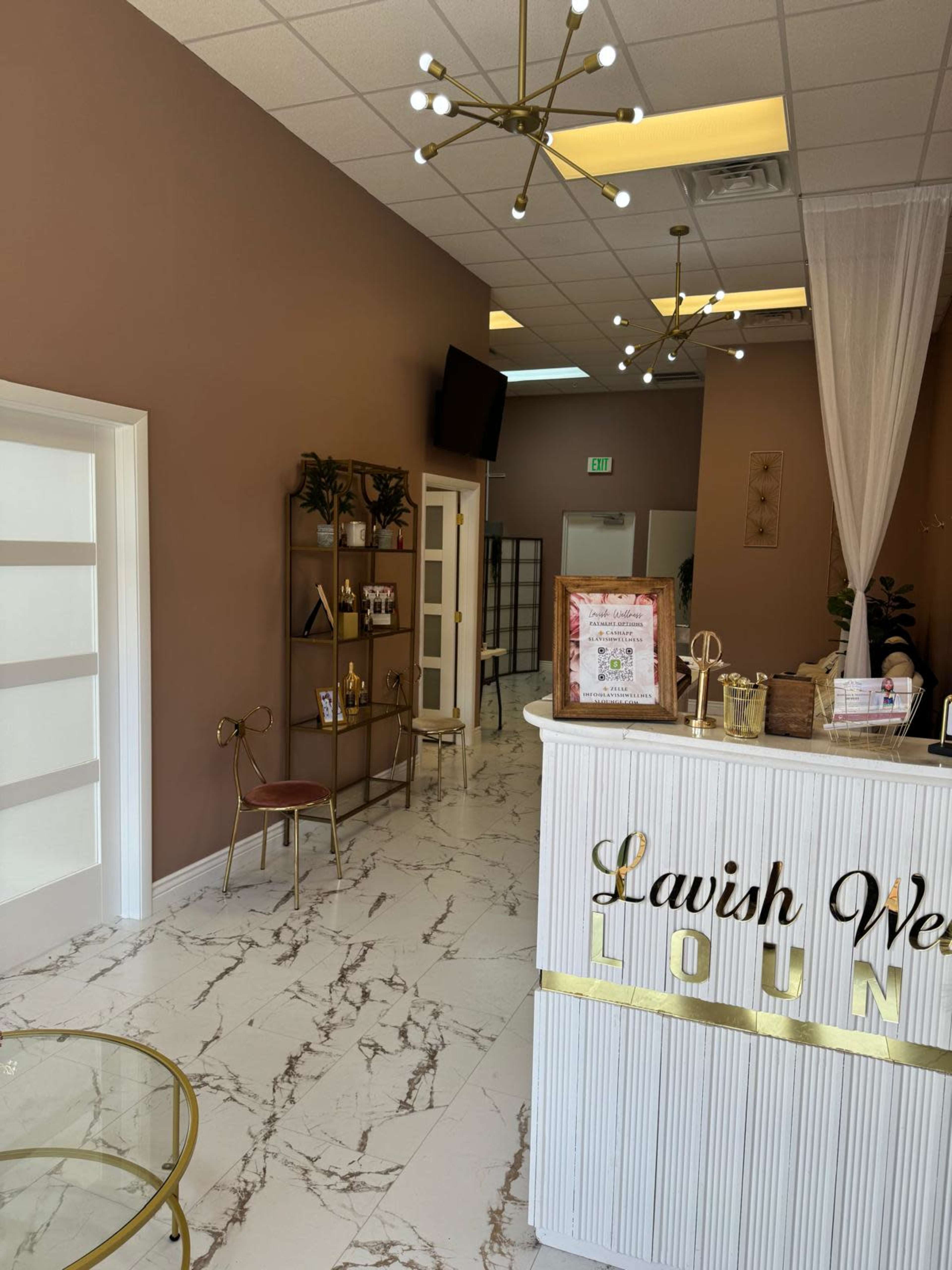 The image shows an interior of a salon or spa with a reception desk, decorative plants, and modern lighting fixtures.