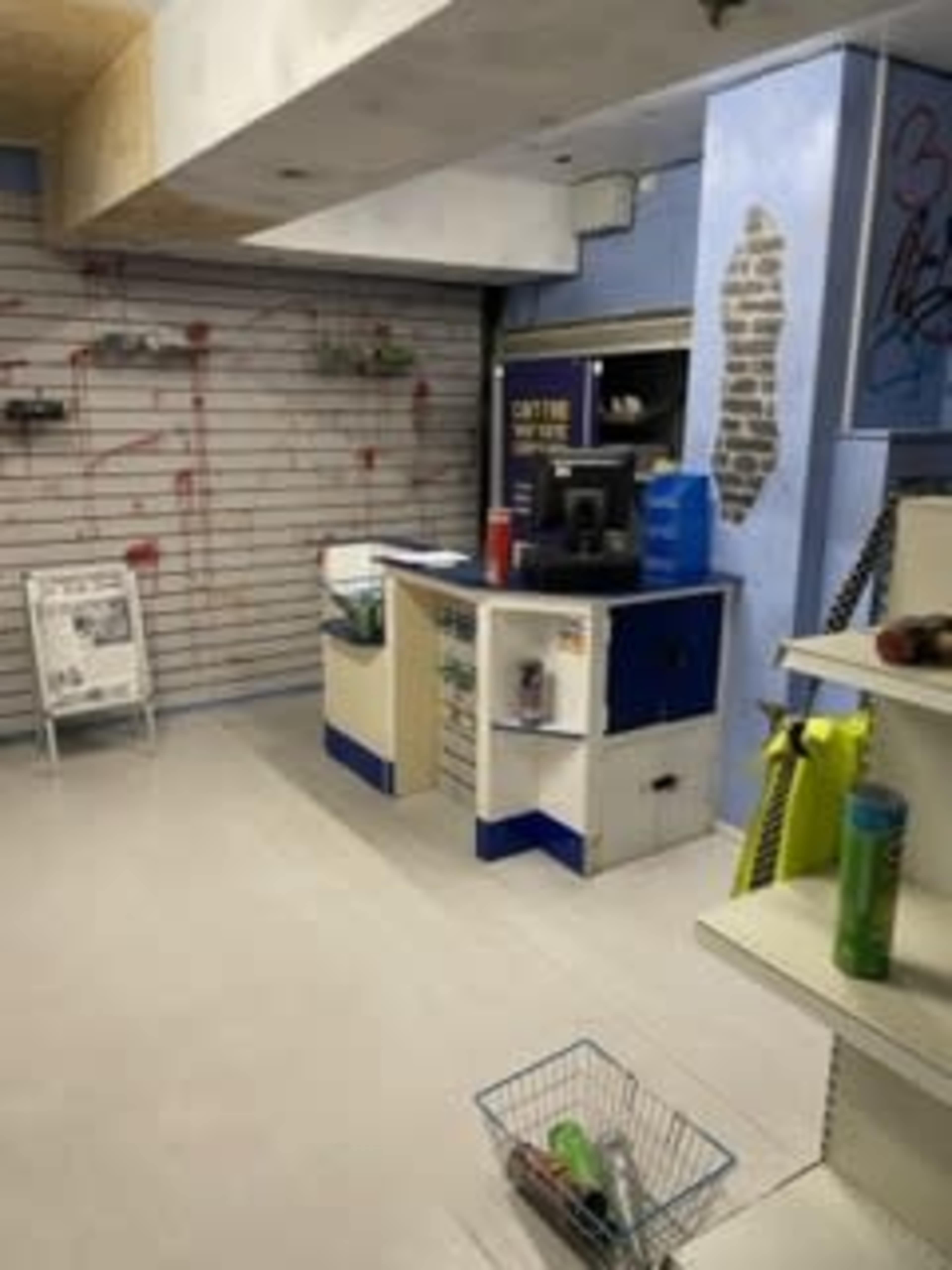 An empty shop interior with a counter, shelves, and items scattered around, along with graffiti and red splatters on the walls.