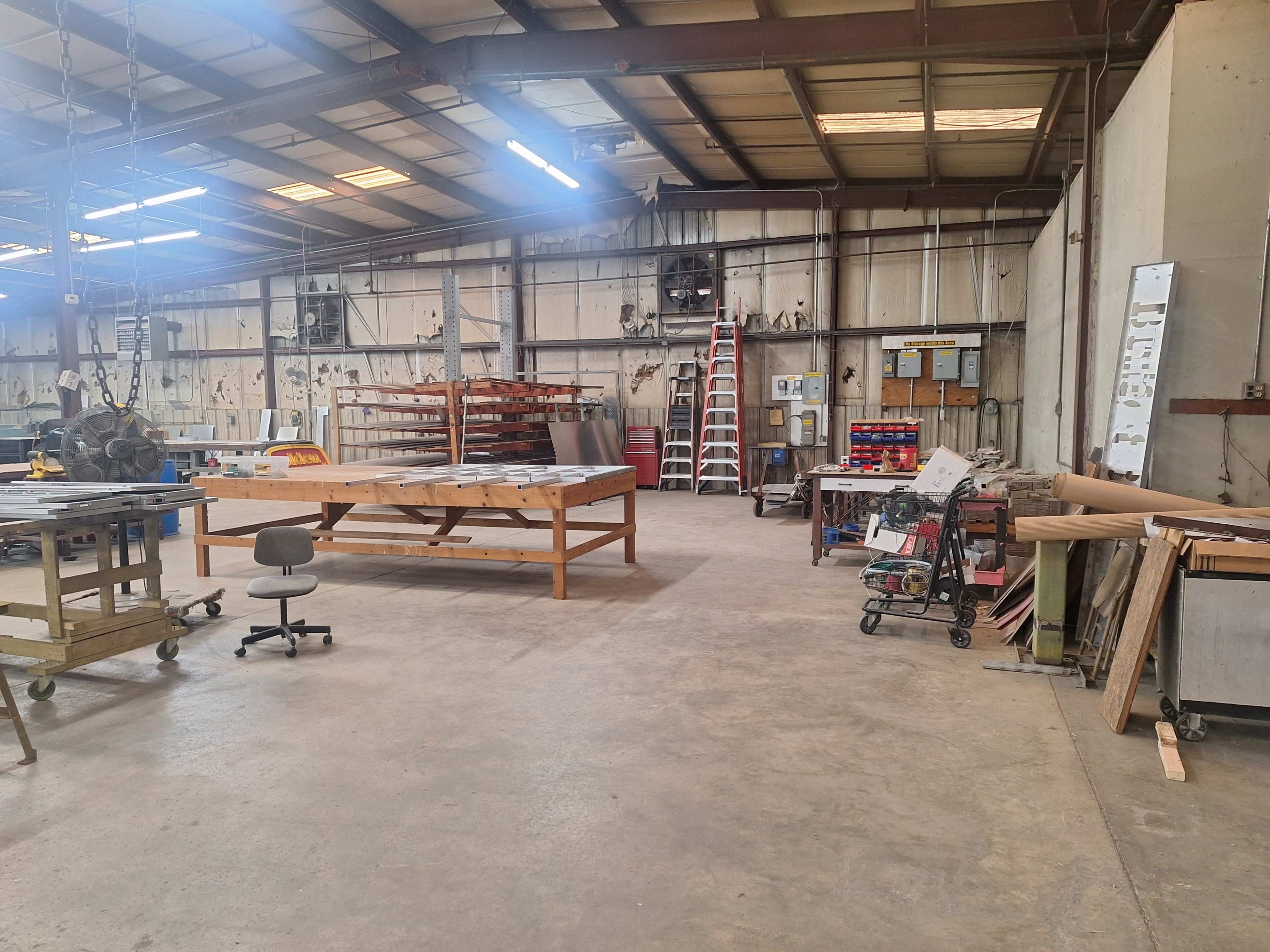 The image shows a spacious workshop with various worktables, equipment, and storage areas filled with tools and supplies.