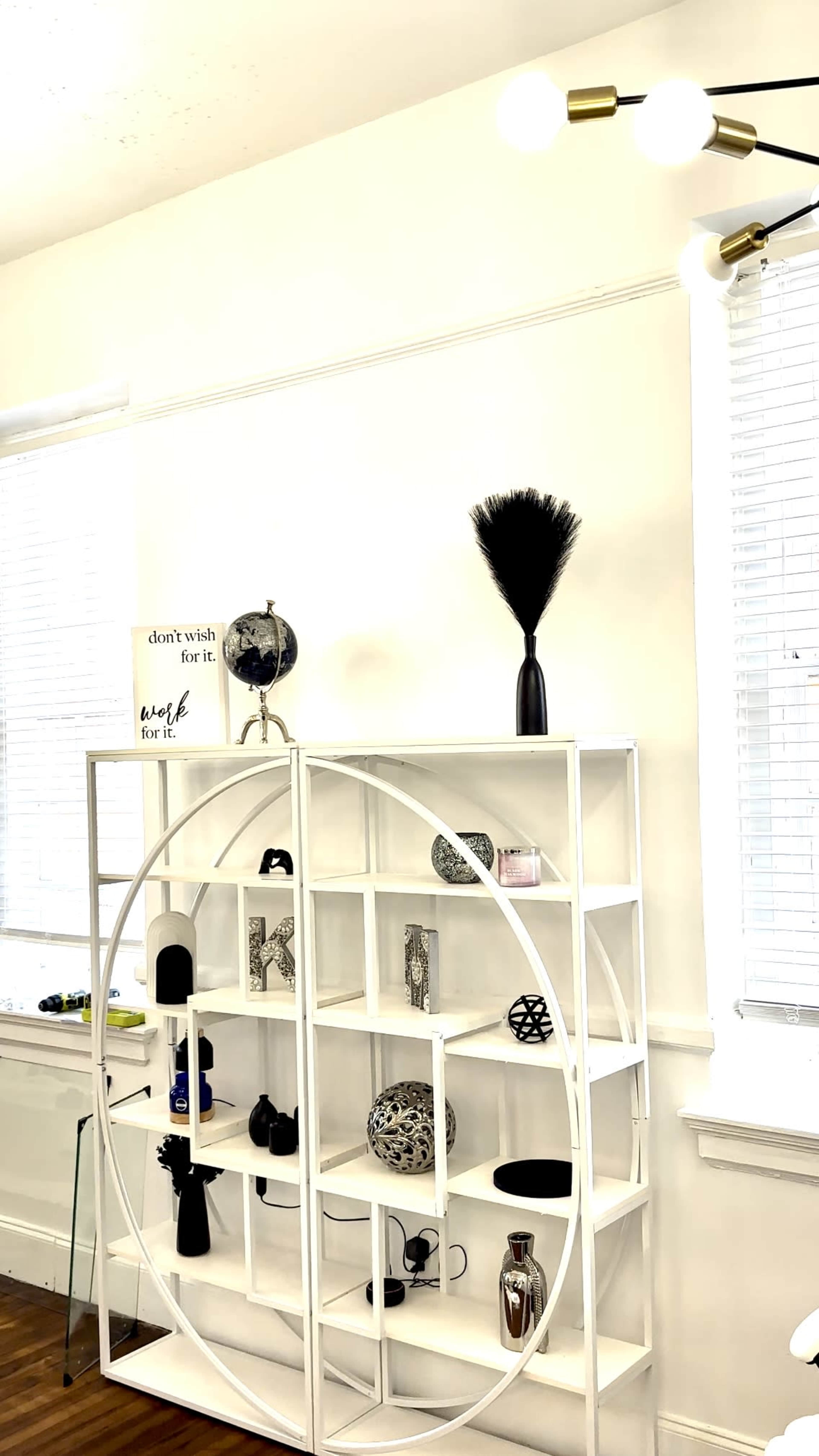 A white shelving unit with circular design displays various decorative items against a light-colored wall.