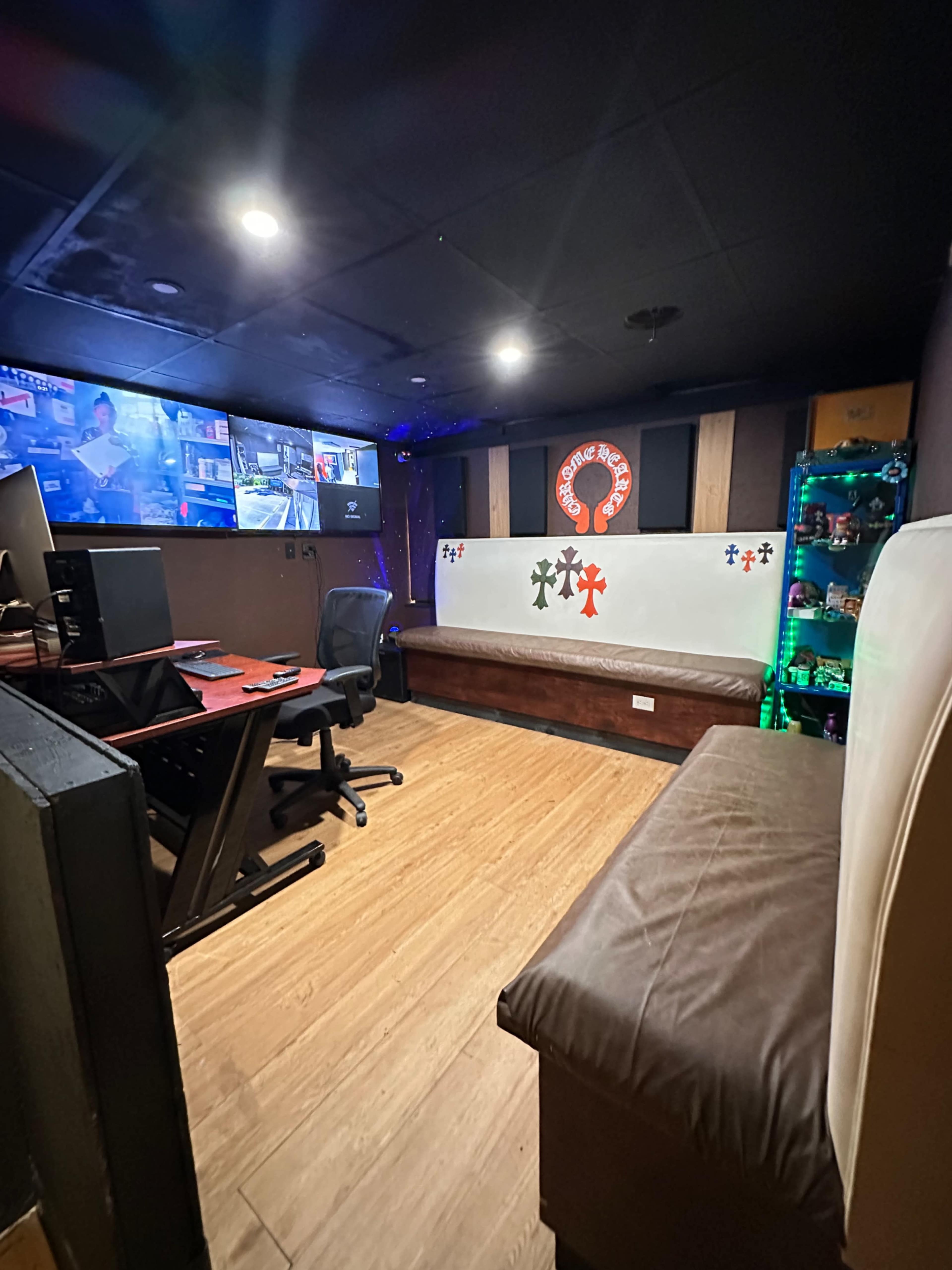The image shows a dimly lit room with a seating area and multiple screens displaying various content along one wall.