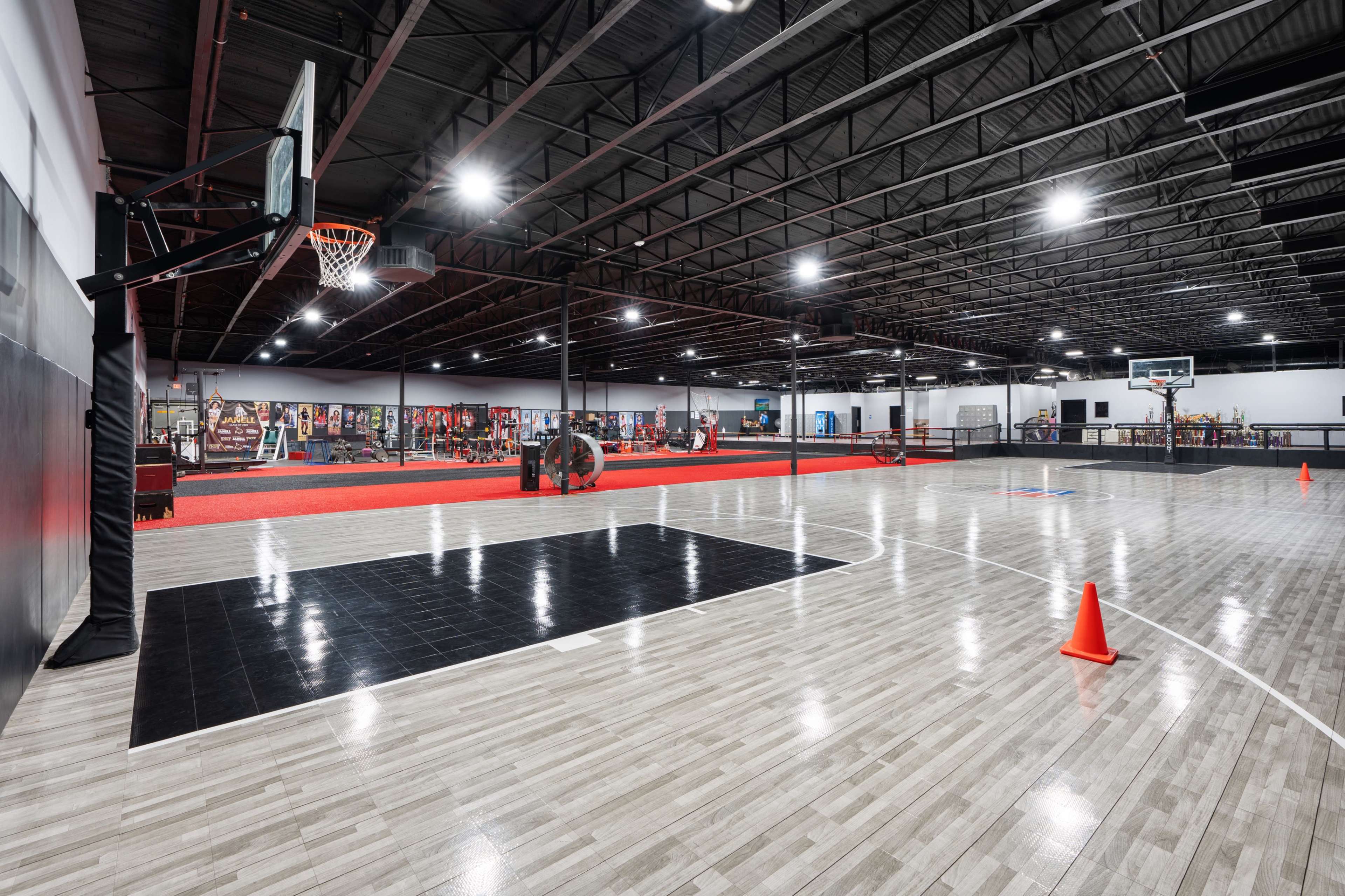 A spacious indoor basketball court with multiple hoops, workout equipment along the walls, and orange cones marking areas on the floor.