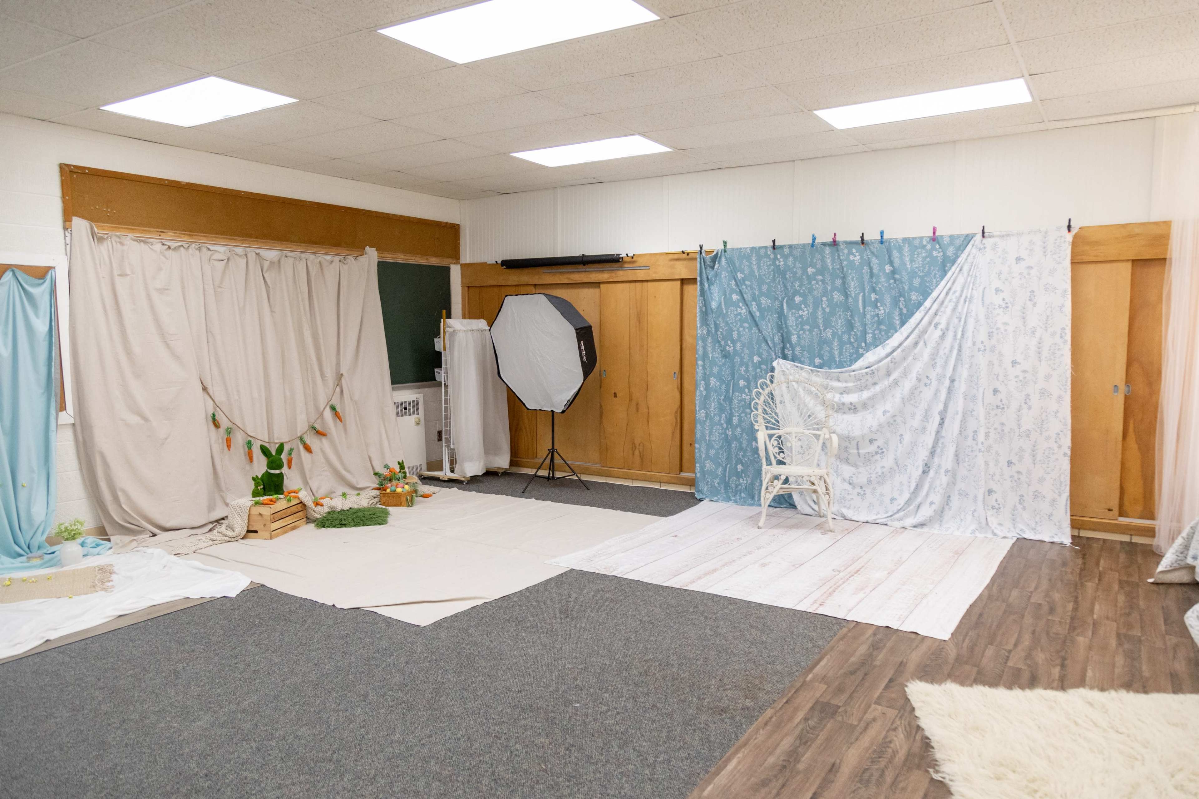 The image shows a spacious room with various fabric backdrops, photography equipment, and decorative elements arranged for a photo session.